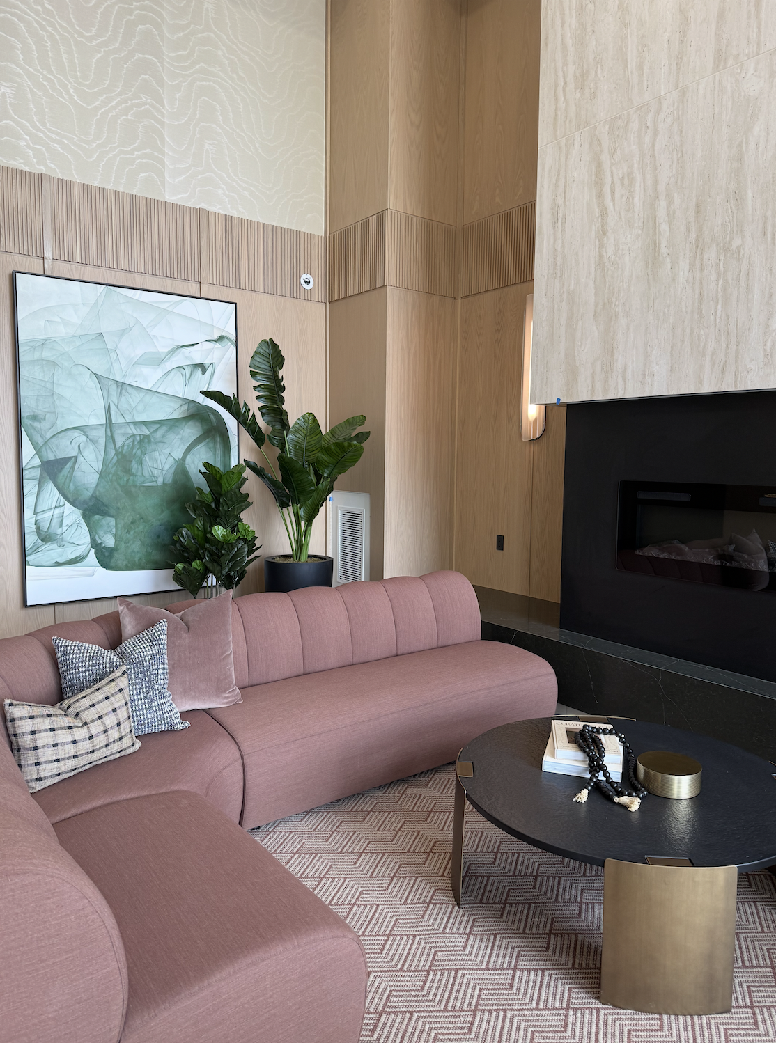 Modern lobby in a professionally designed new construction apartment building with pink sofa, faux plants, and a black coffee table, and abstract art on wood walls.