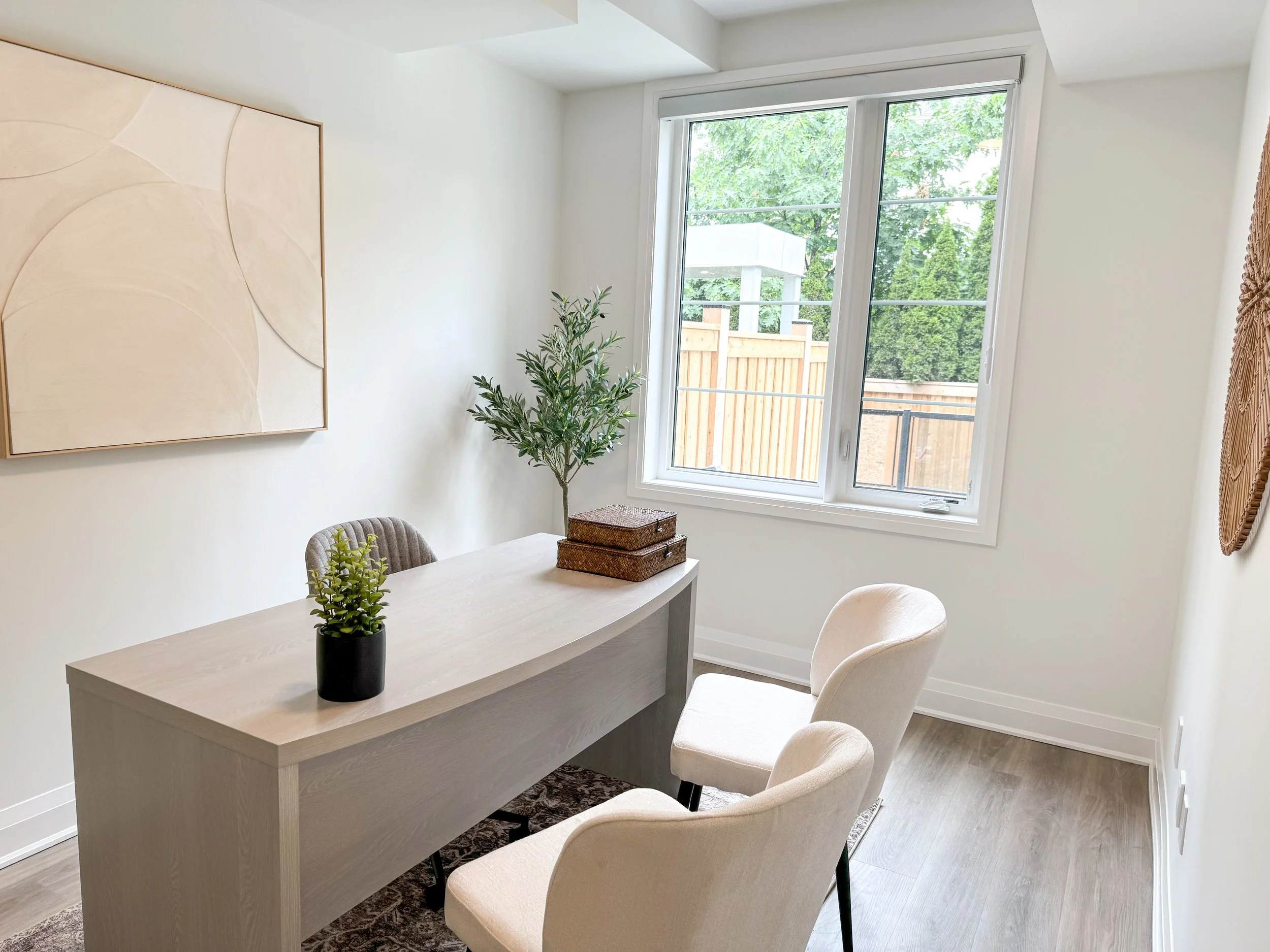 Modern leasing office with a grey desk, white chairs, modern decor, a faux plant, and minimalist artwork..