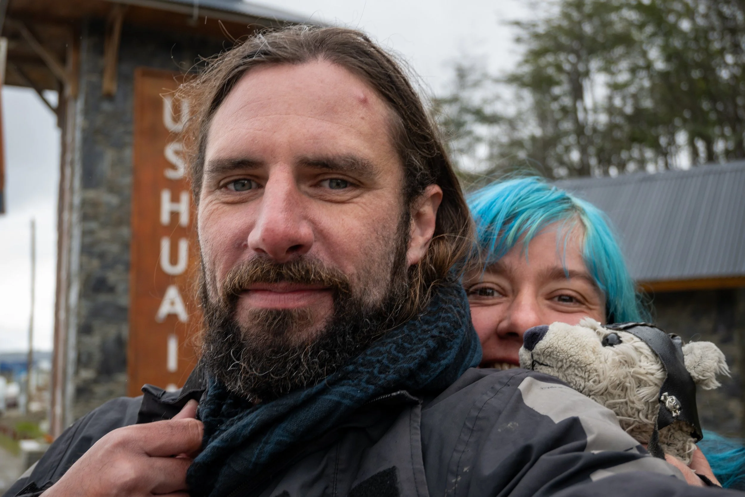 Smiling couple and their mascot at the Ushuaia entrance pillars
