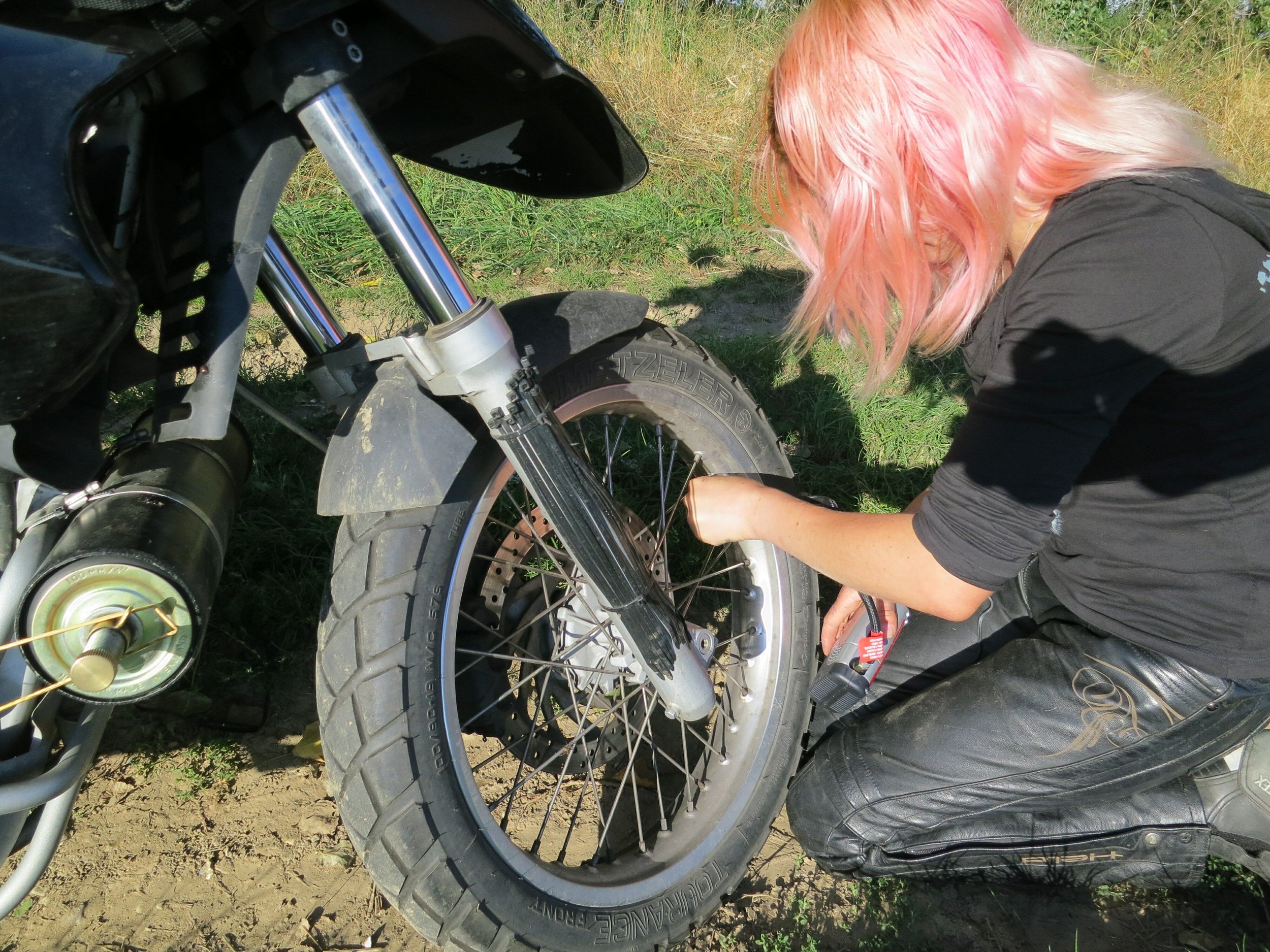 girl with pink hair checking the motorcycle tire pressure
