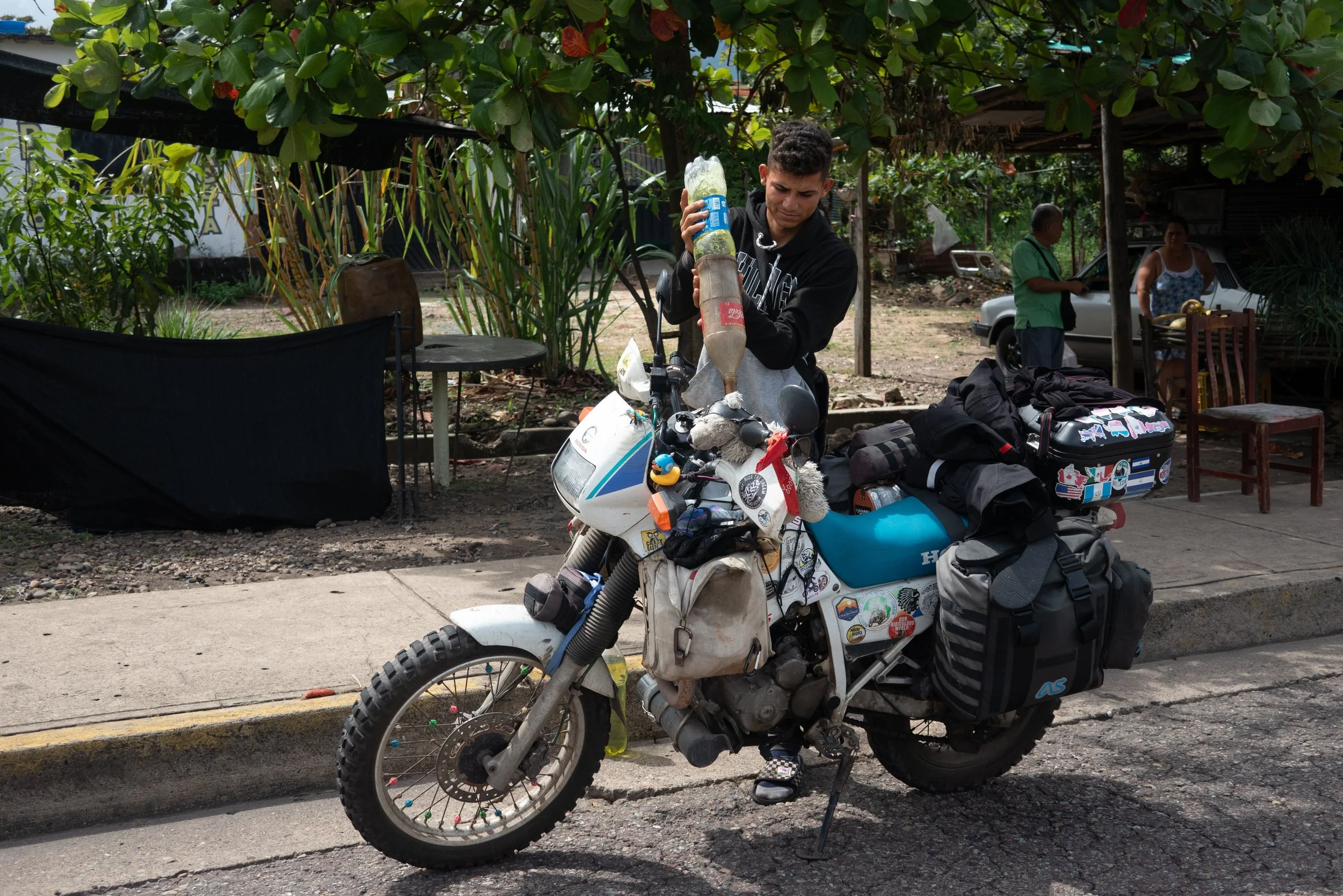 young man pouring petrol from soda bottles into a motorcycle tank