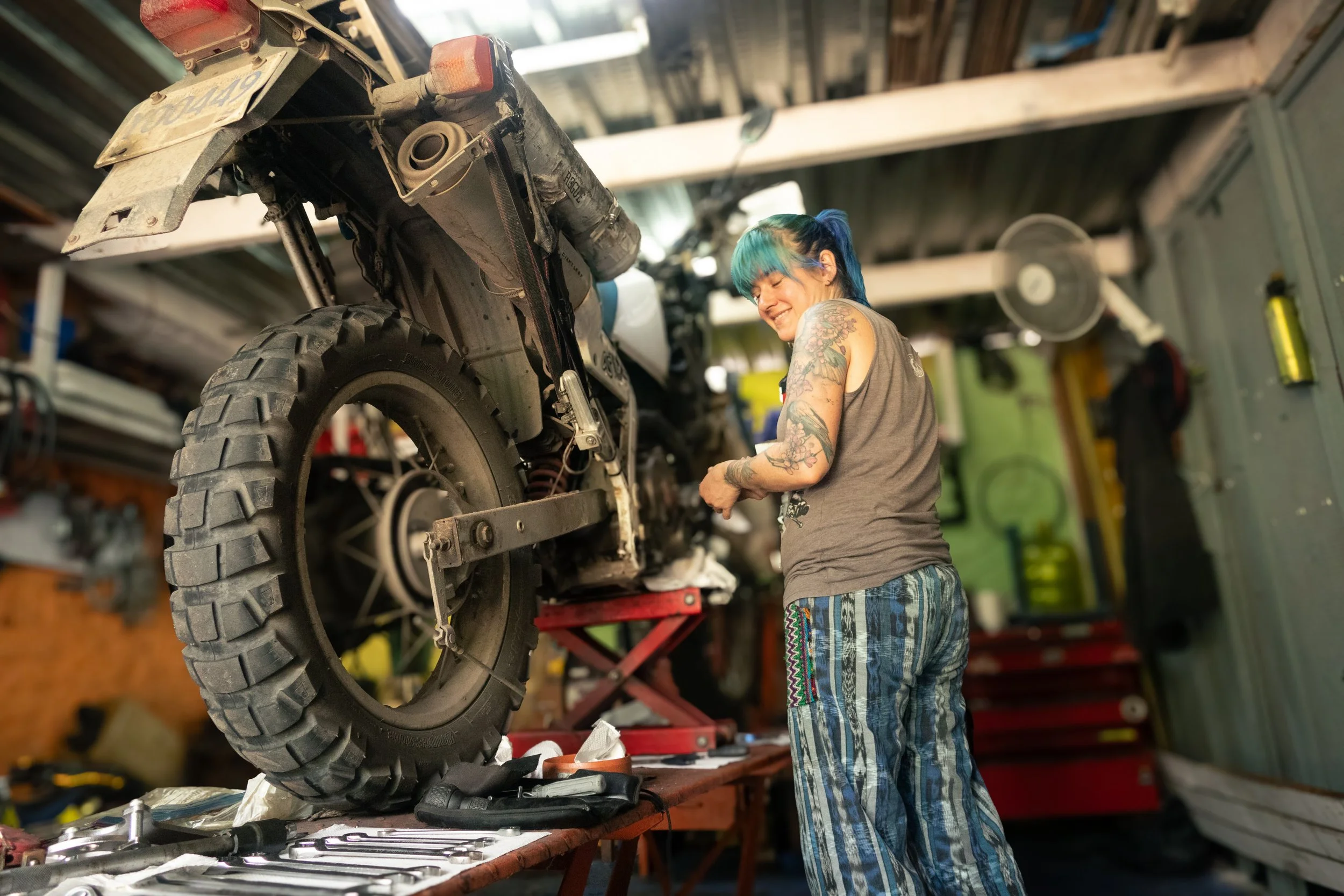 woman motorcycle mechanic working on a bike that's up on a hoist