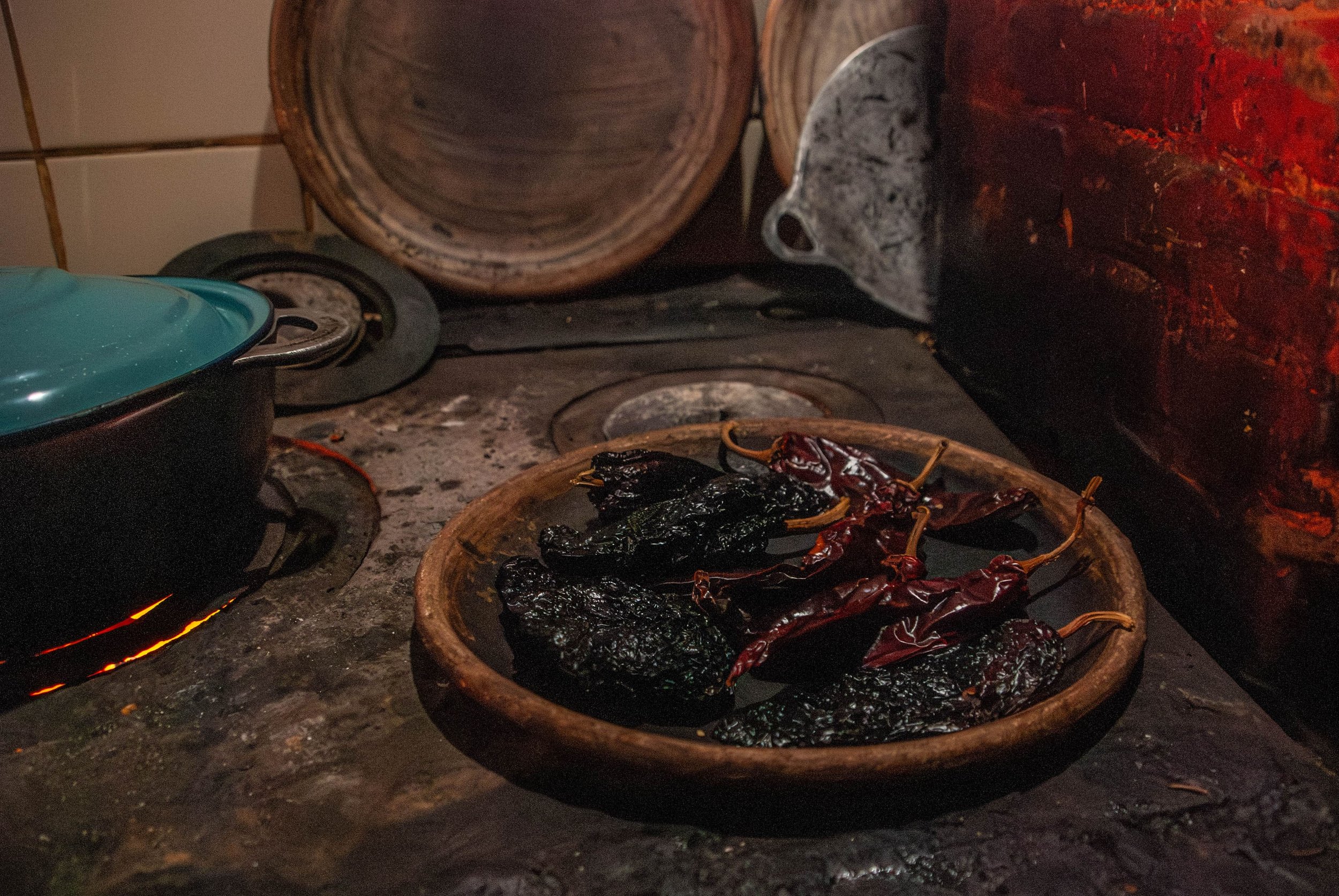 Chiles asándose sobre una sartén de barro y una estufa de leña para preparar pepian guatemalteco | ¿Por qué las clases de cocina en Antigua Guatemala son una experiencia que no te puedes perder?