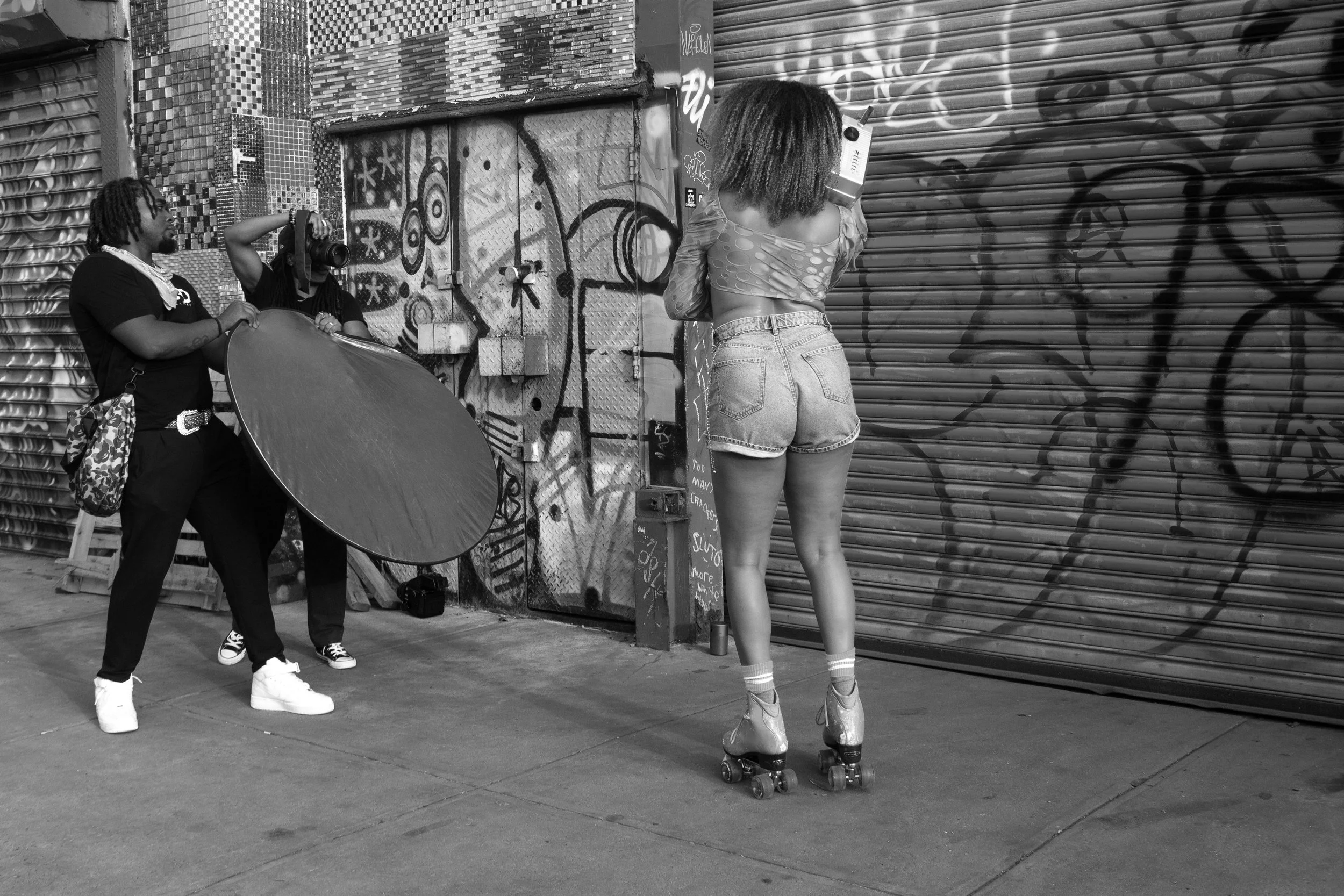 Boogie Down Cinema crew members hold up a reflector and a camera as they capture a model on roller skates holding a boombox.