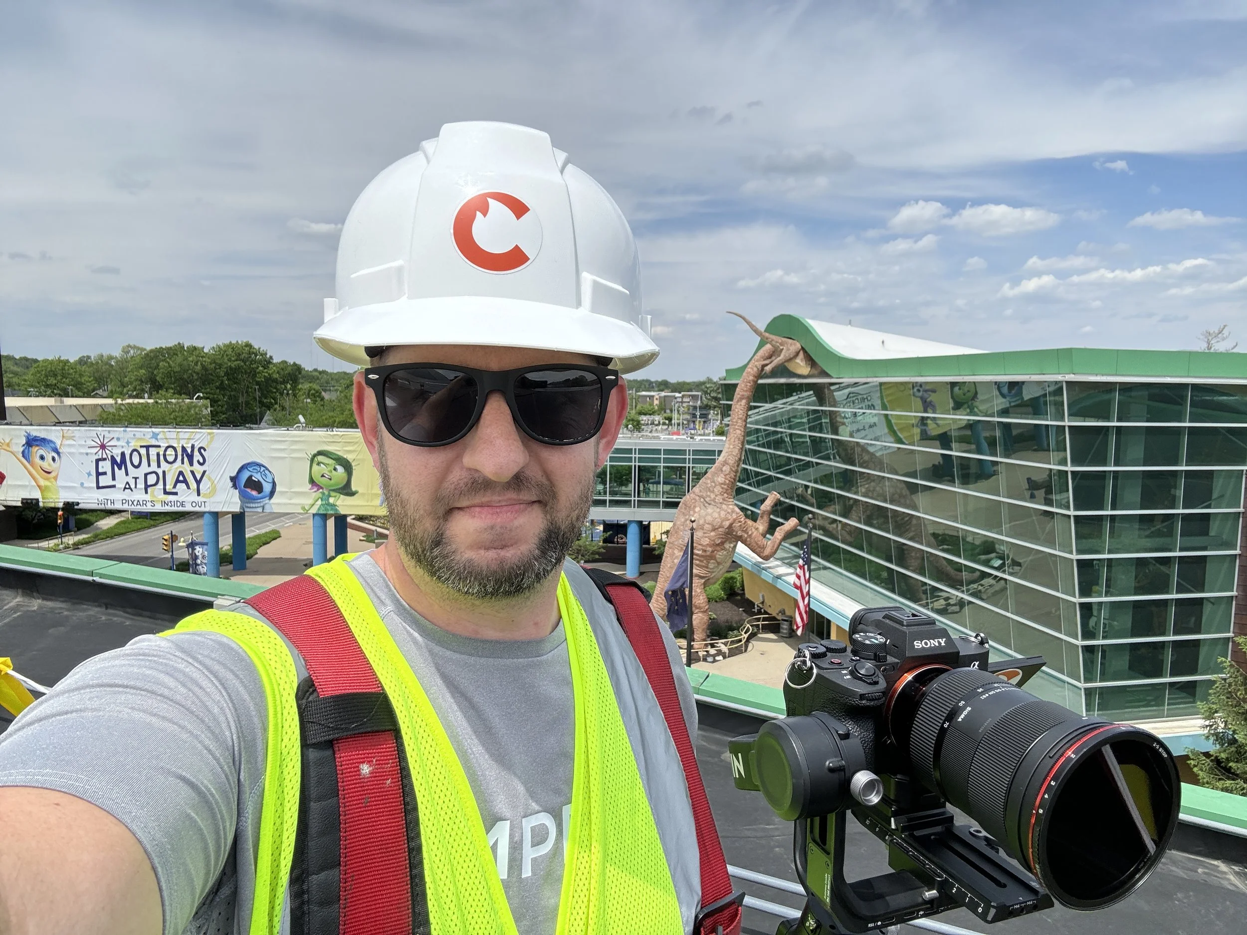 An Indianapolis videographer wearing construction gear holding a camera on top of the roof of the Children's Museum in Indianapolis where he was creating content for the roofing company.