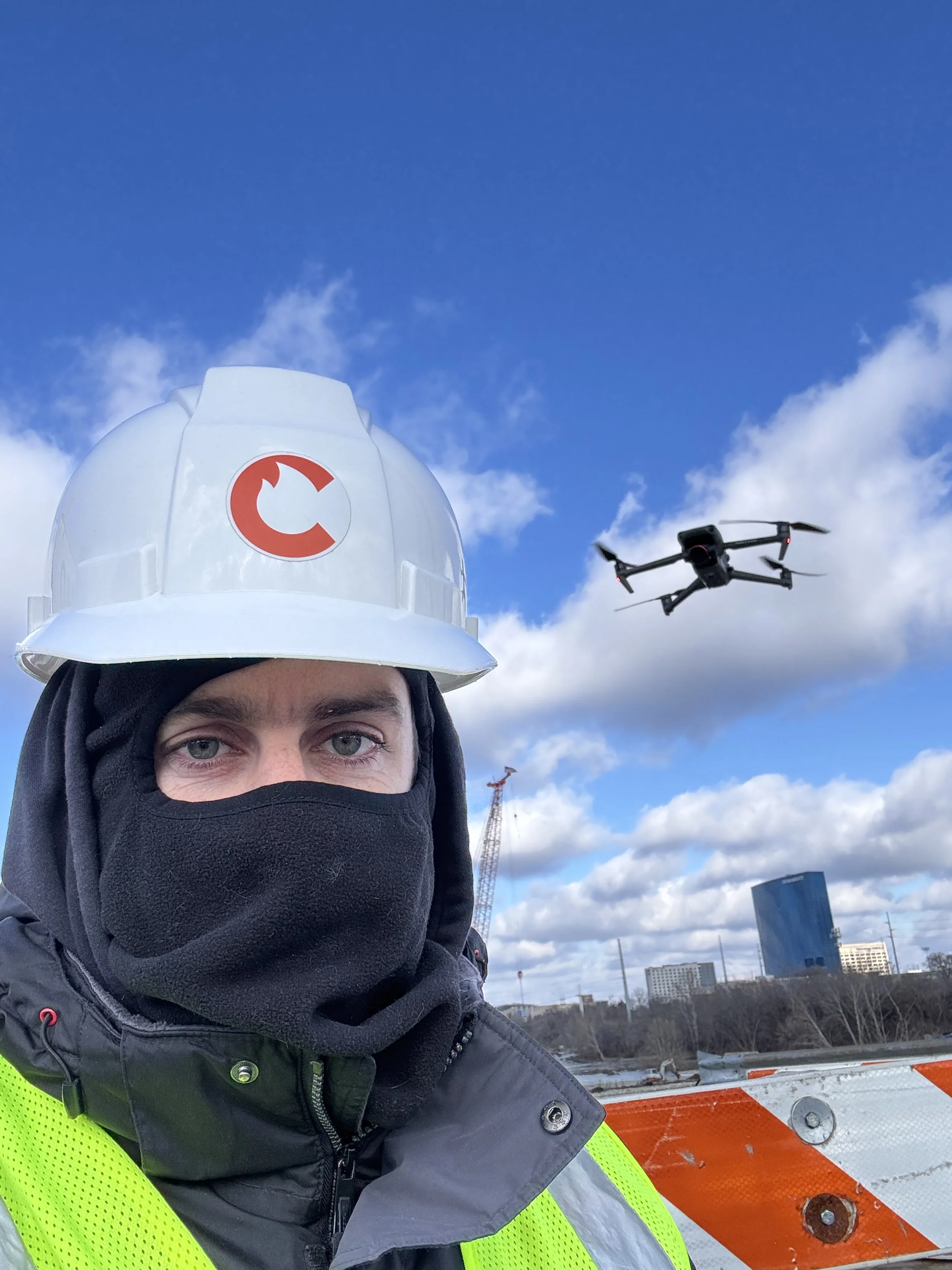 An Indianapolis drone pilot wearing a hard hat while flying a drone at a construction site to capture photos and videos of the construction project.