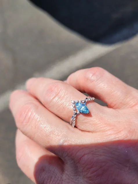 An elegant blue diamond infinity ring worn on a hand.