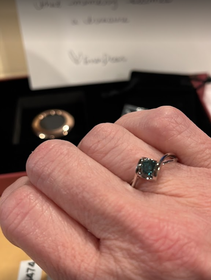 Hand wearing a silver ring featuring a deep blue diamond, set in a unique twisted band design.
