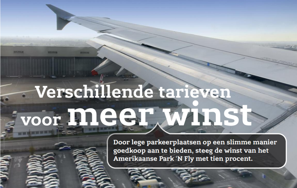 Foto van een vliegtuigvleugel genomen vanaf het raam in een vliegtuig, vlogen over een parkeerterrein vol auto's met een luchthavengebouw op de achtergrond.