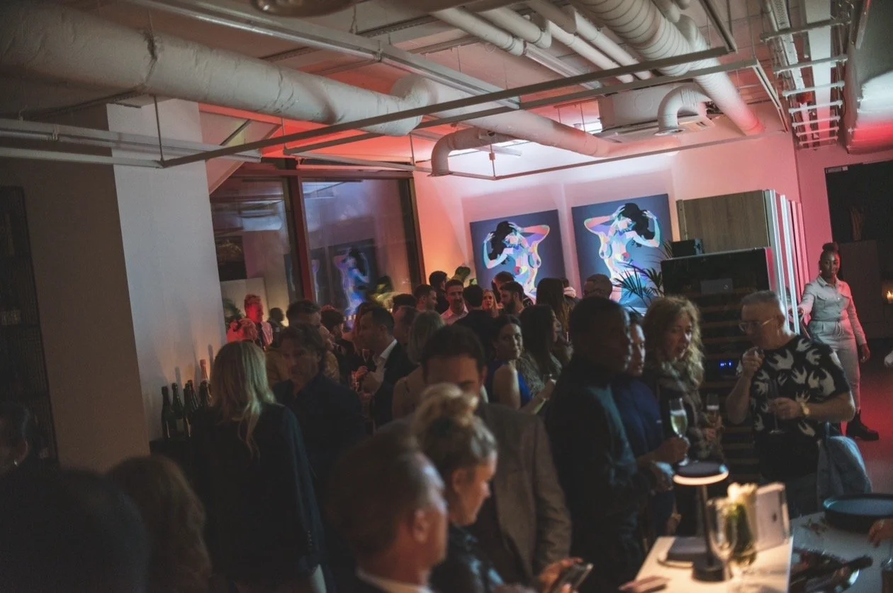 People gathered at a social event or party in an indoor venue with modern decor, artwork, and colorful lighting.