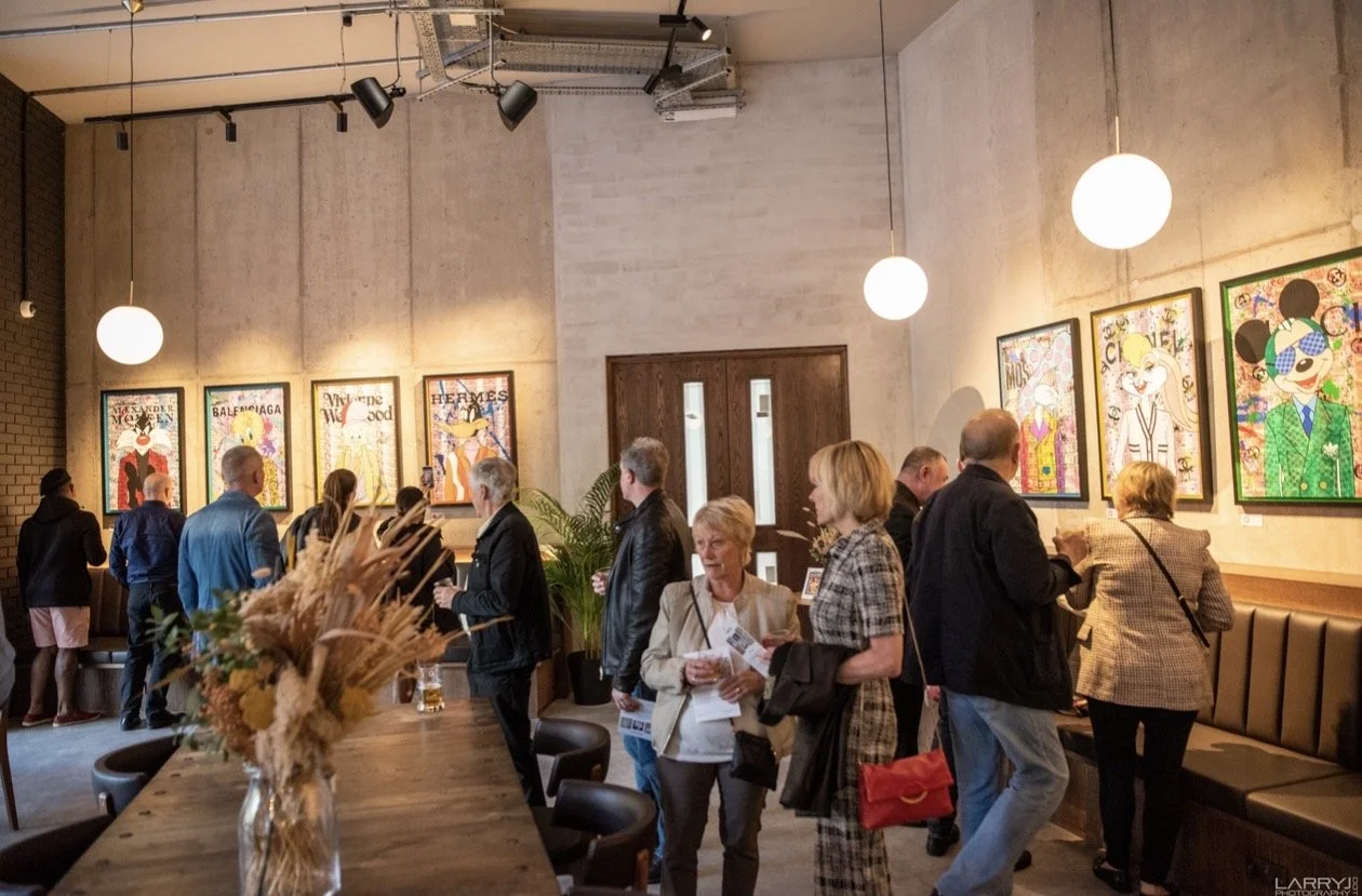 Art gallery with colorful pop art portraits of famous fashion icons displayed on the wall, visitors engaging and viewing the artwork.