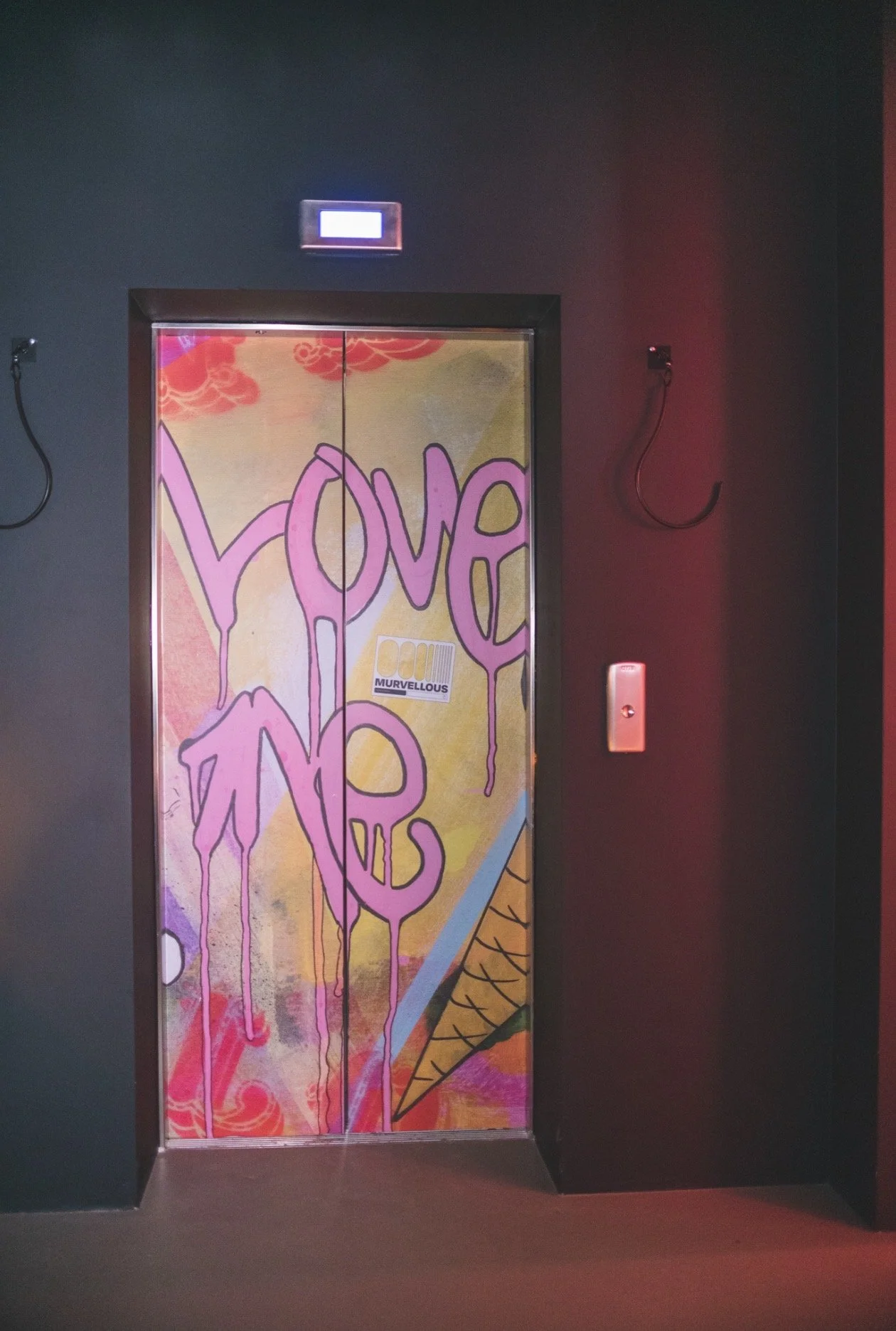 Colorful elevator door with graffiti-style art and the words 'Love' and 'Me' written in large pink letters, with an ice cream cone illustration on the right side.