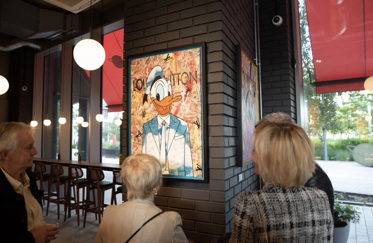 A group of people inside a modern cafe or restaurant, standing and looking at a colorful, graffiti-style painting.