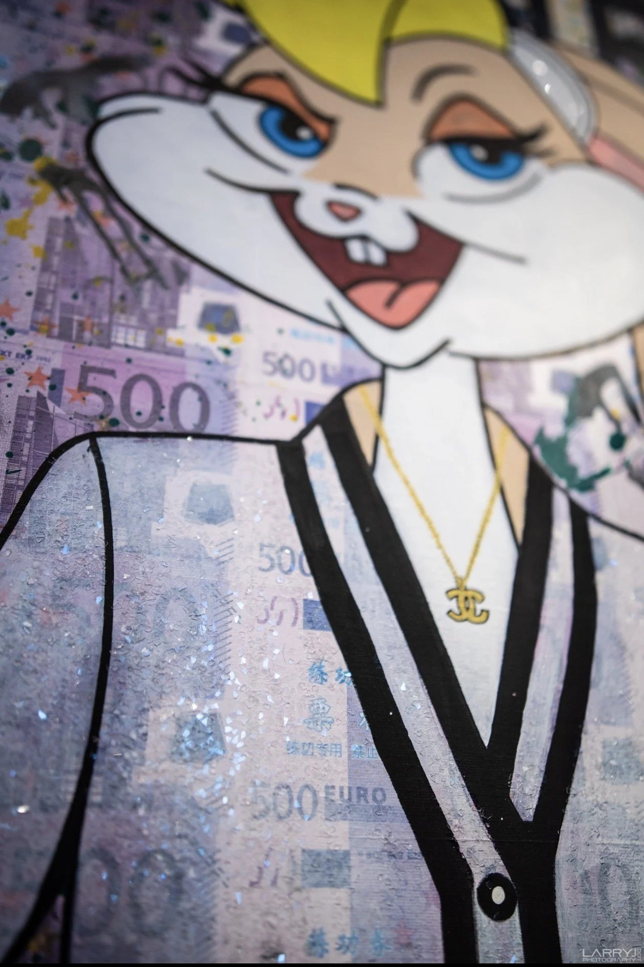 A cartoon character with blonde hair, blue eyes, and a big smile, wearing a black and white suit with a gold necklace, superimposed on a background of 500 euro banknotes with crushed glass.