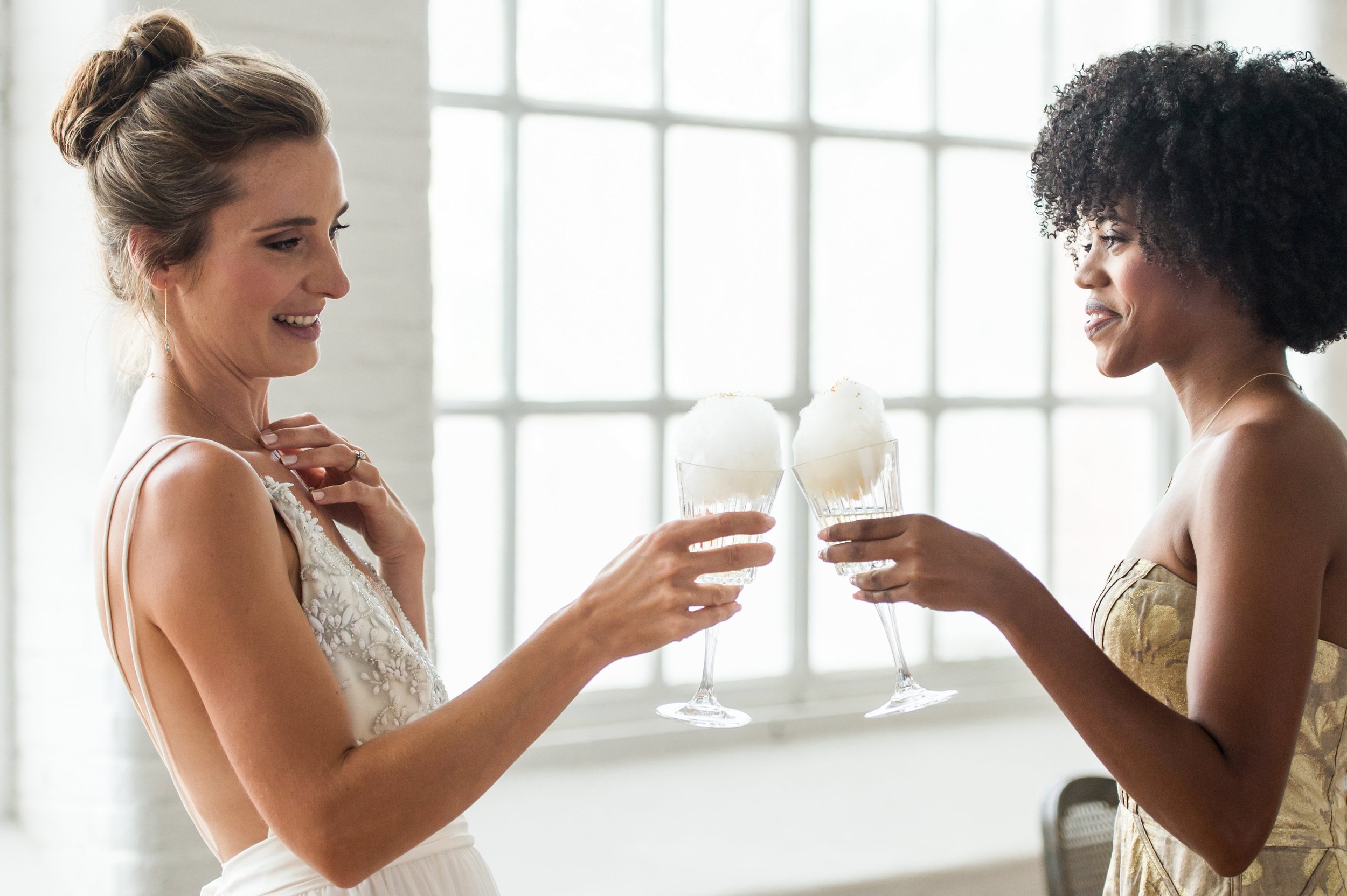 A bride and bridesmaid hold champagne glasses from our Boston cotton candy cart