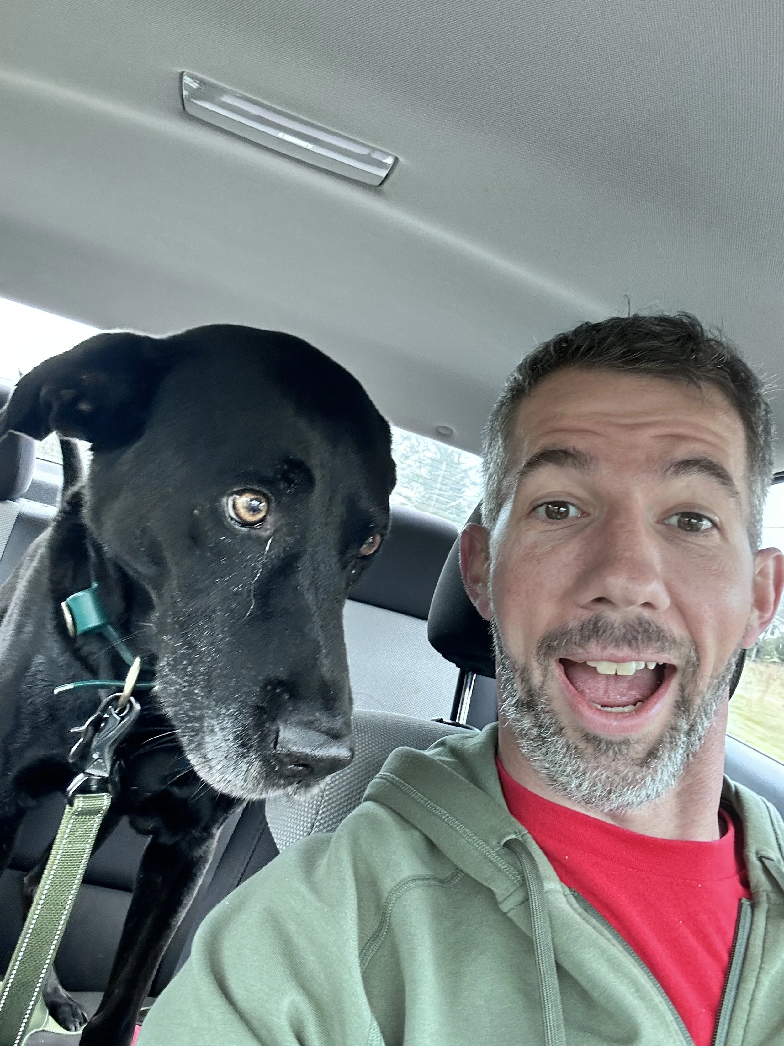 A man and a black dog taking a selfie in the backseat of a car.
