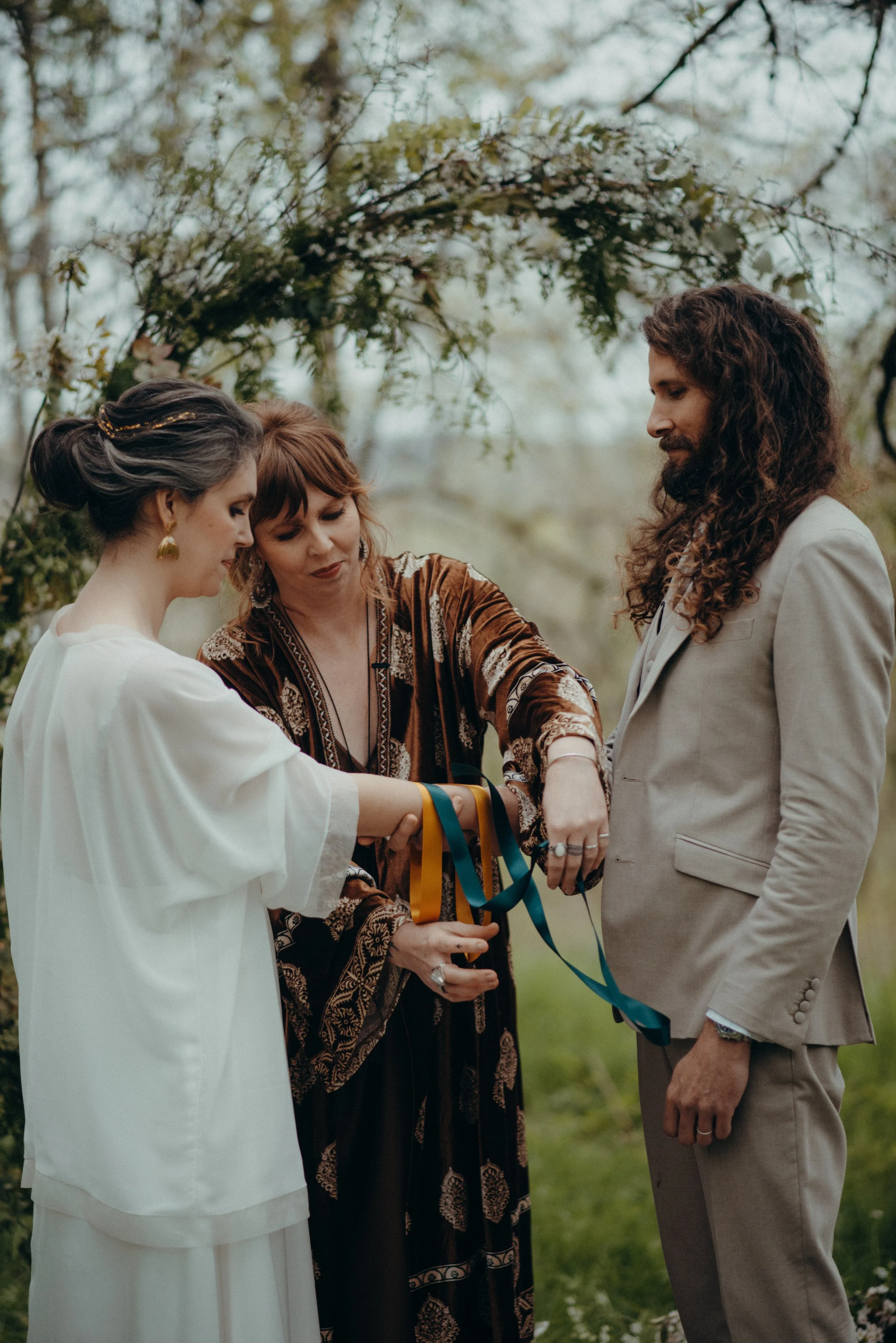 Rituel de handfasting dans les Hautes-Pyrénées célébré par Judith La Dame de Cœur : un couple en costume participe à la cérémonie en plein air, la femme tenant des rubans colorés.