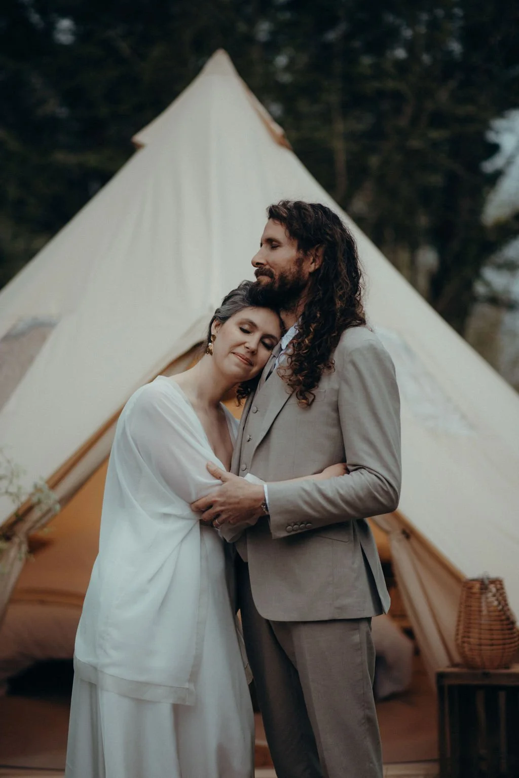 Mariage pleine nature Cérémonie de mariage alternatif célébrée par Judith La Dame de Cœur : un couple heureux s’embrasse devant une tente beige en plein air, exprimant amour et tendresse dans la nature