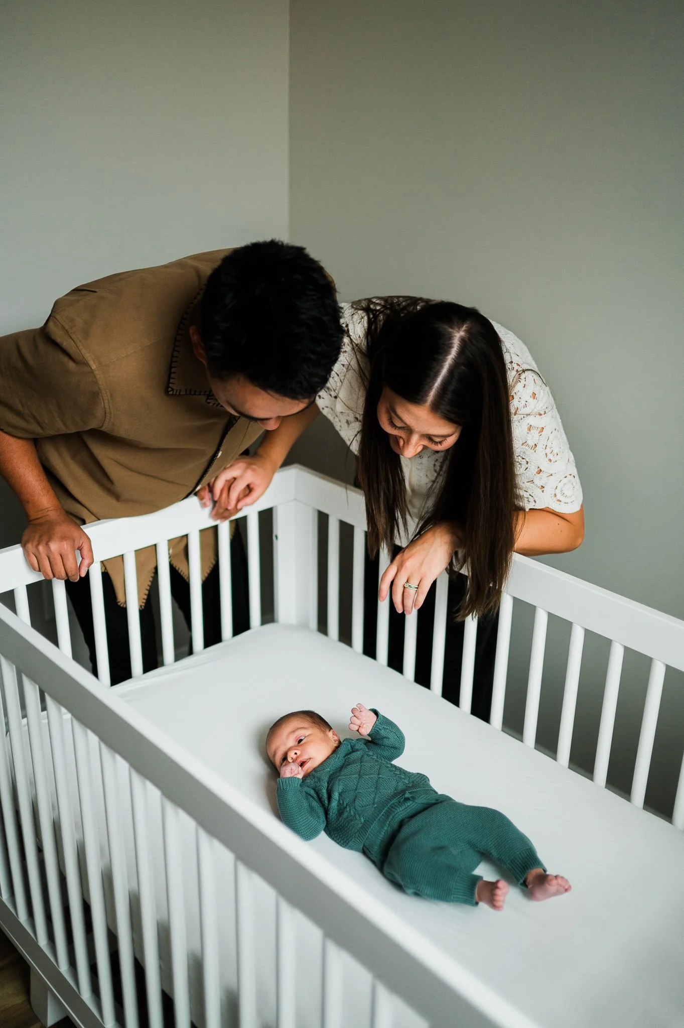 Parents looking into a crib at their baby lying inside.
