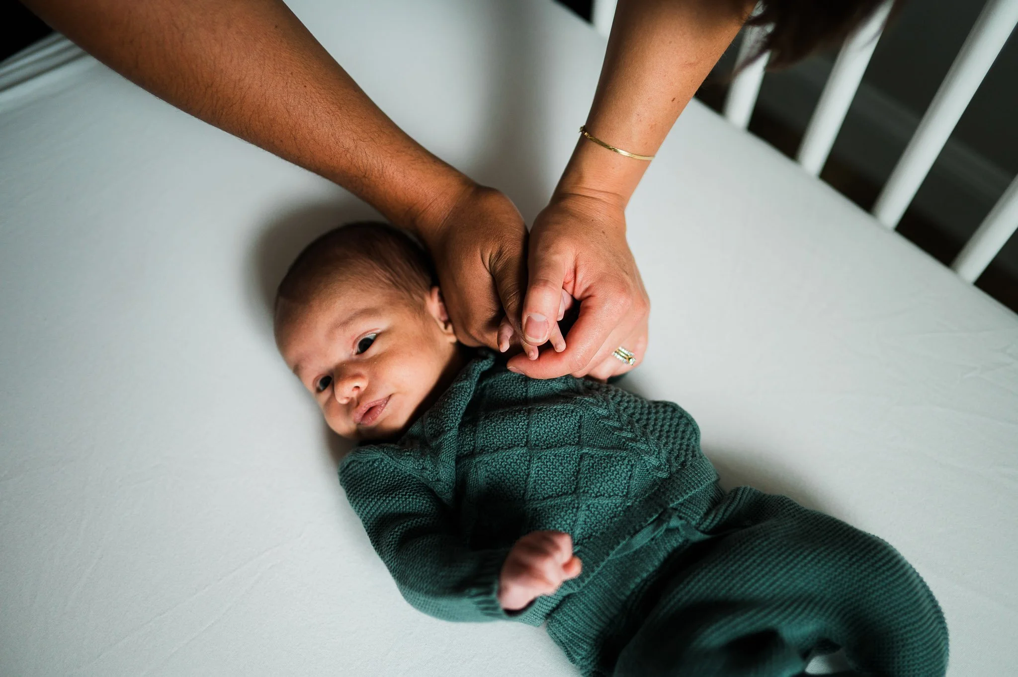 Close-up of a baby lying on a changing table, being gently held by two adult hands.