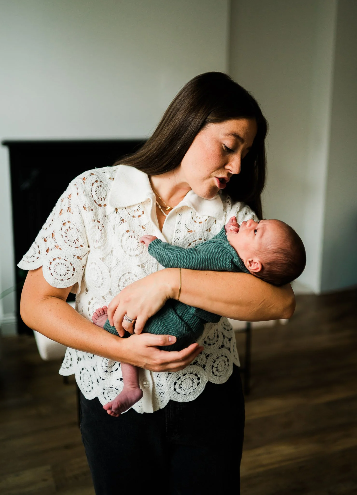 A woman holding a baby in her arms, looking down at the baby with affection indoors.