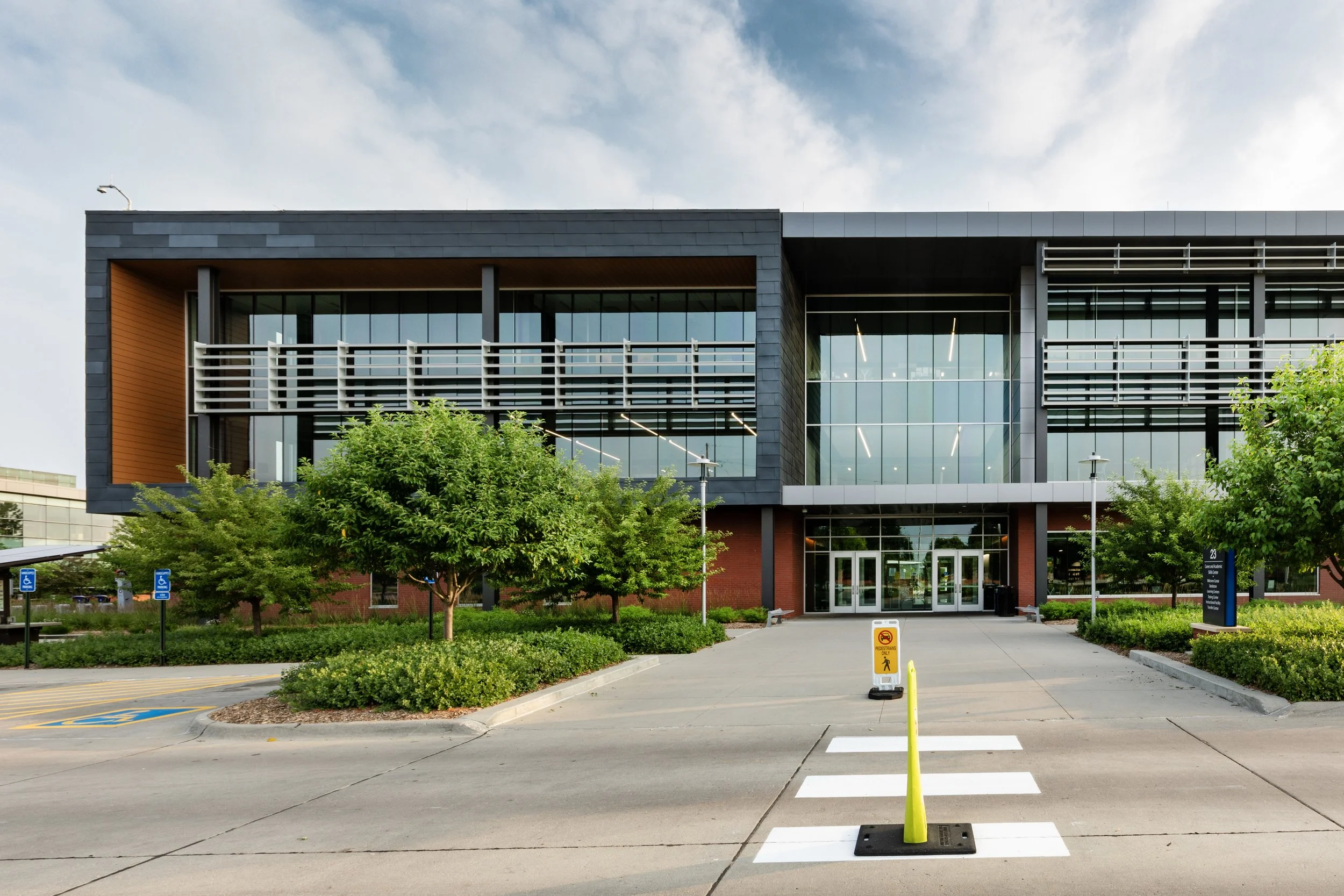 Modern glass-fronted building with trees and a crosswalk in front, overcast sky.