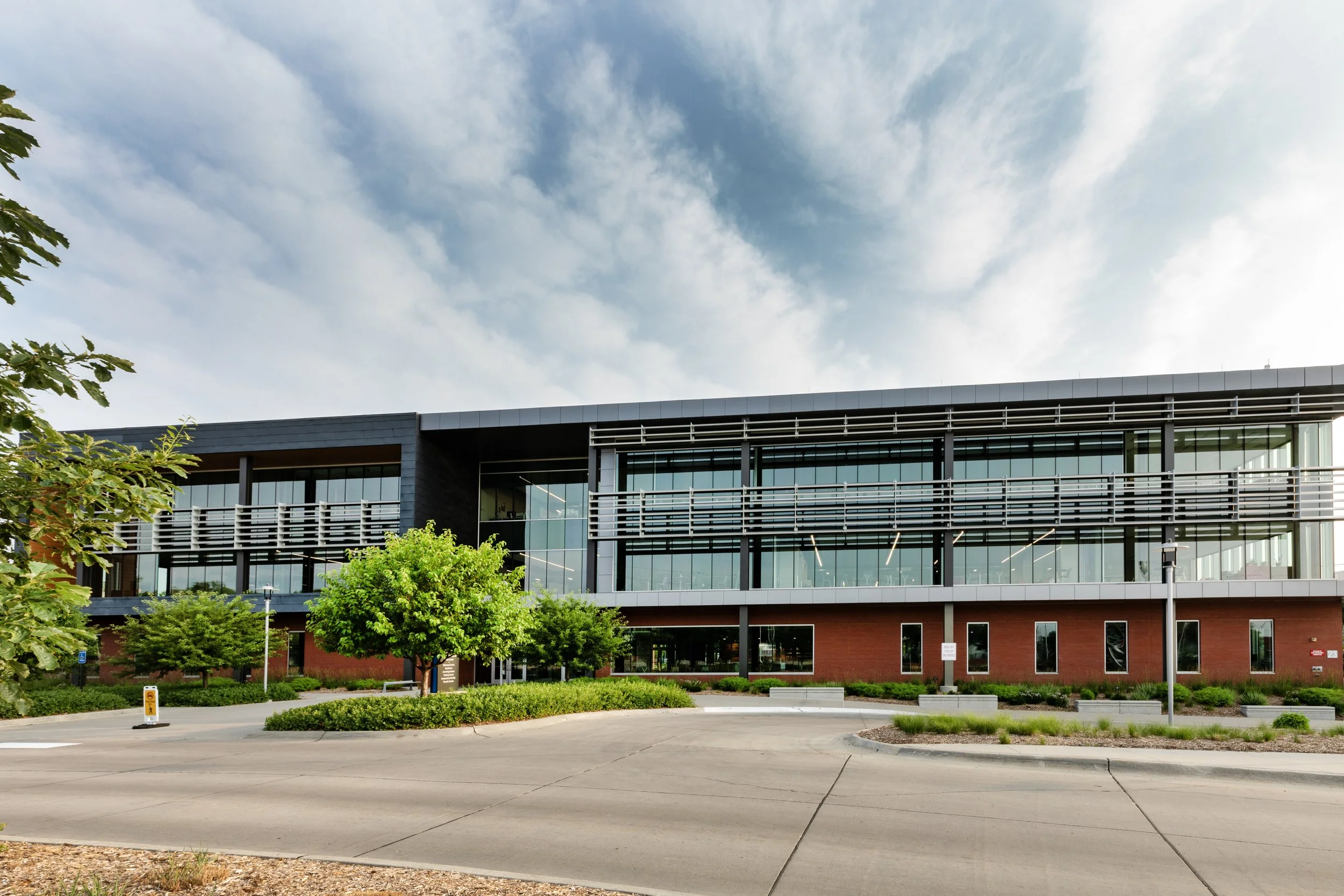 Modern office building with glass facade and landscaped surroundings under a cloudy sky.