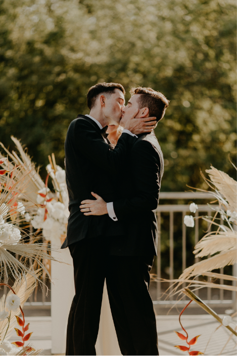 Two grooms kiss in front of large floral arrangements at their wedding planned by Minneapolis wedding designers