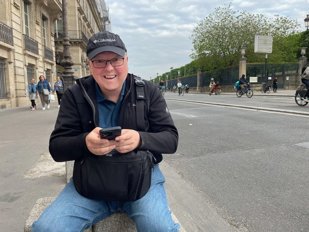 John checking his phone in Paris