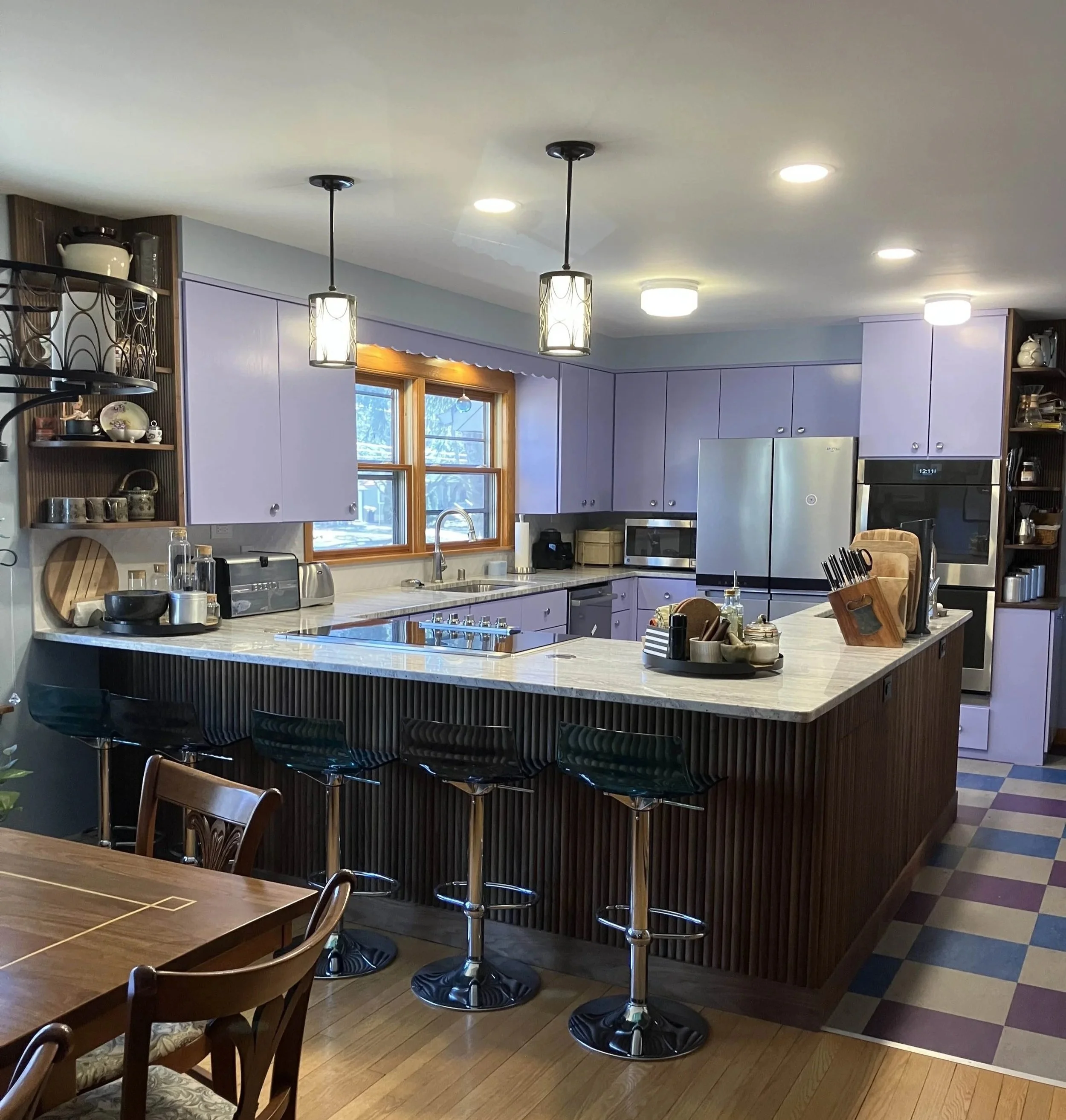 Kitchen with purple cabinets, a marble island with black bar stools, and a window overlooking trees.