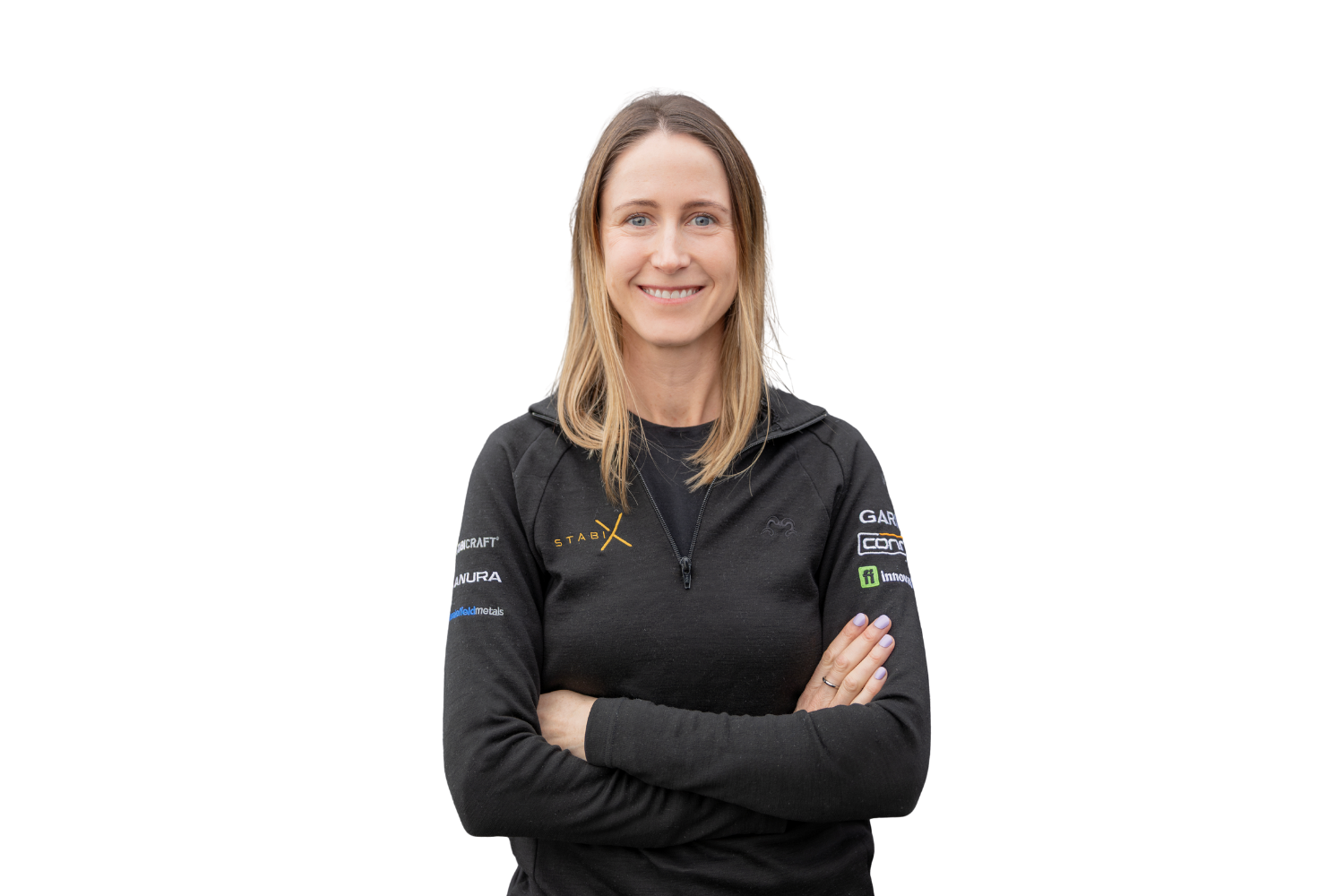 A woman with long blonde hair, smiling, wearing a black zip-up jacket with various sponsor logos on the sleeves and chest, standing in front of a black background with a white geometric design.