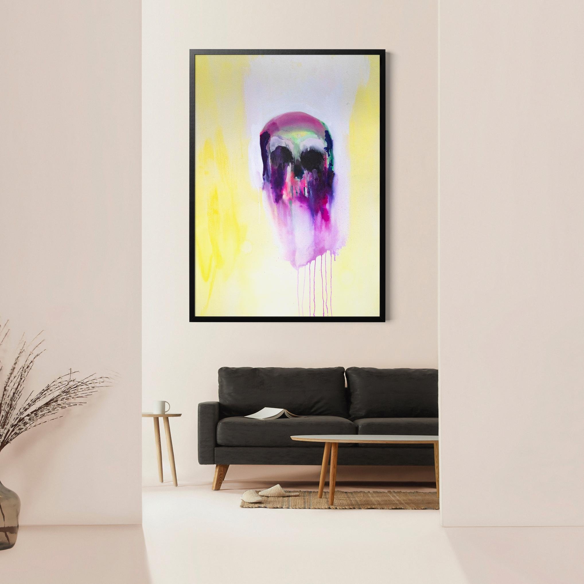 Framed abstract skull artwork on a pastel wall above a black couch, blending moody purples and drips with a radiant yellow background.