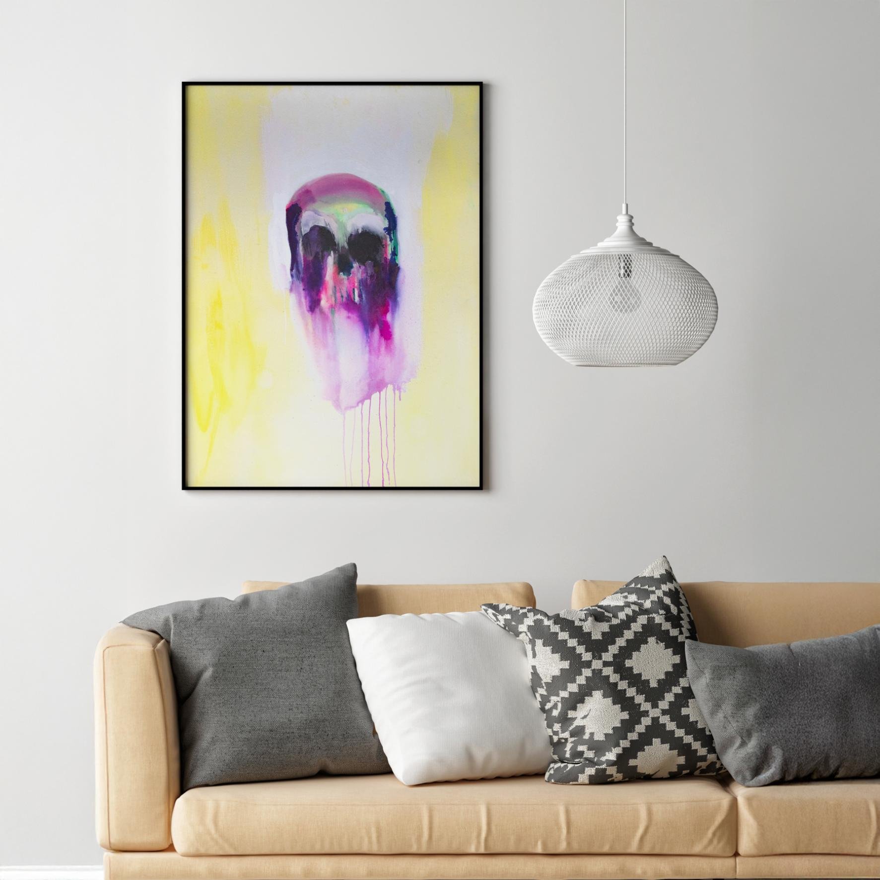 Skull painting in black frame hanging above a beige couch with monochrome pillows, bringing vivid purples and yellows into a clean, modern space.