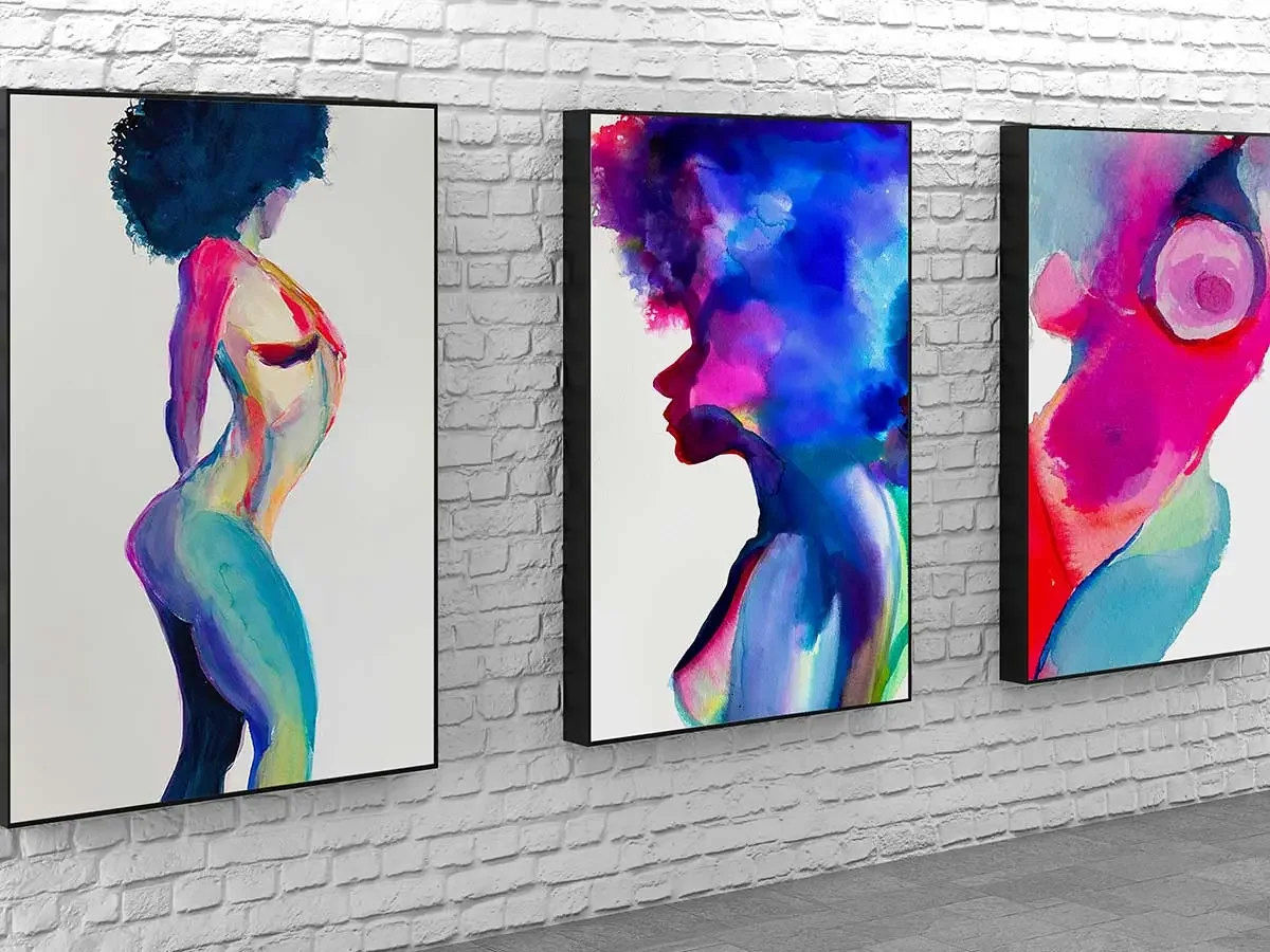 Three colorful abstract watercolor paintings of a nude woman with an afro hairstyle displayed on a white brick gallery wall, featuring vibrant pink, blue, and purple tones with expressive brushstrokes.