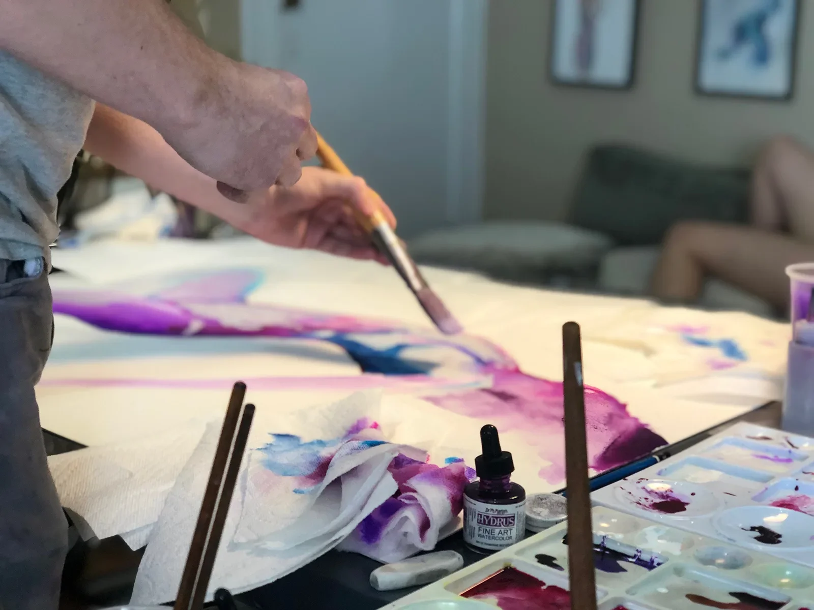 Artist Nick Horvath painting a colorful watercolor figure artwork using brushes and ink on large paper.