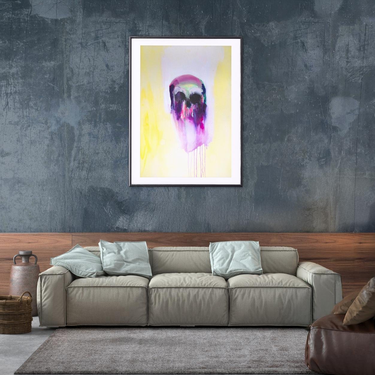 Skull painting in black frame hanging above a beige couch with monochrome pillows, bringing vivid purples and yellows into a clean, modern space.