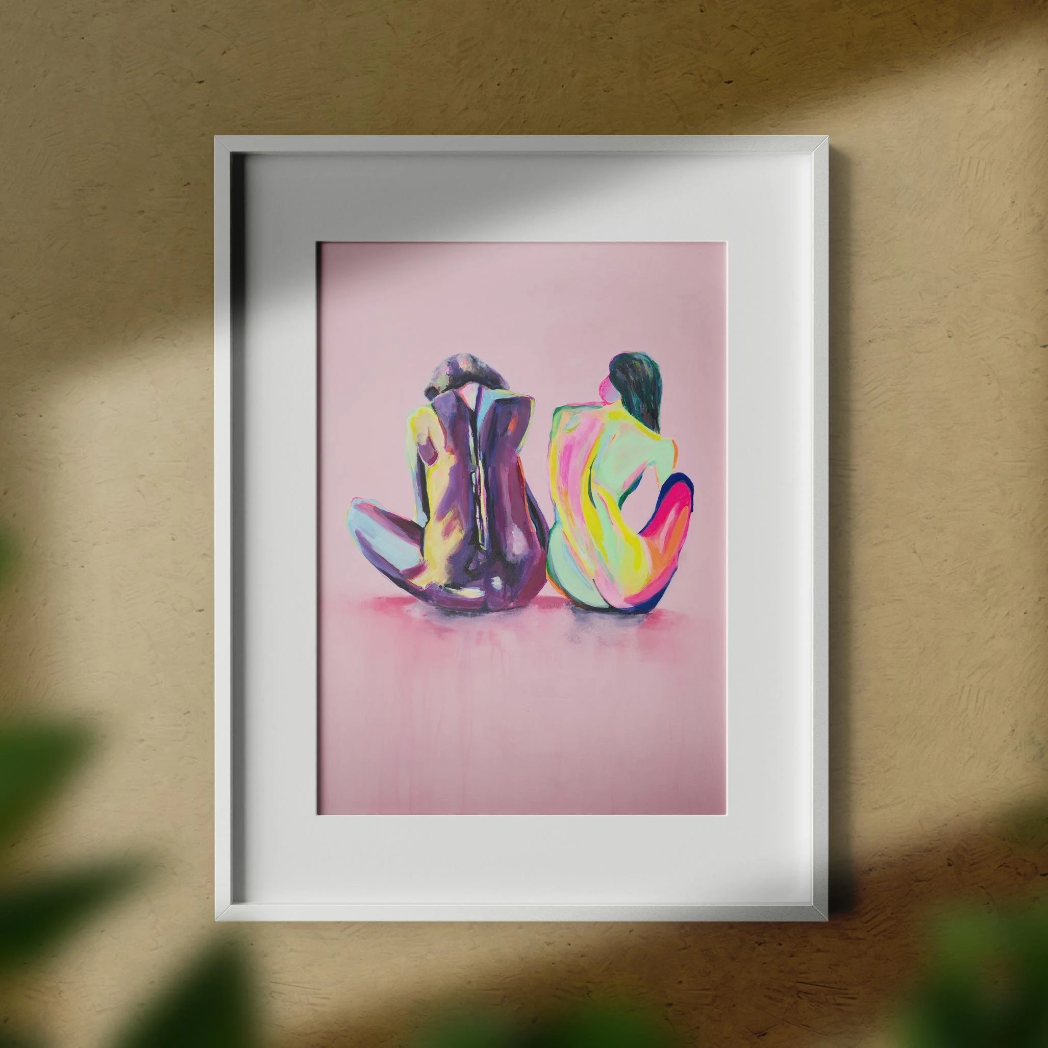 Soft-focus view of the “Friends” painting framed in white and hung on a textured beige wall, bathed in warm daylight with gentle shadows.