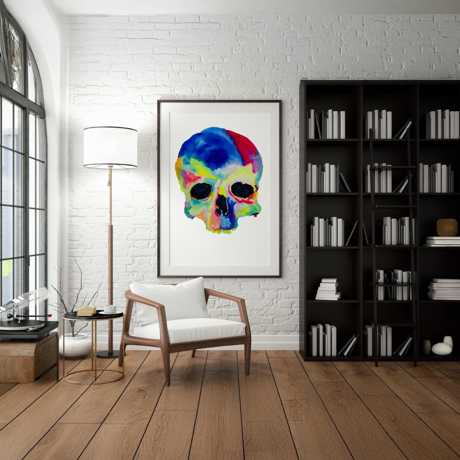Framed vivid skull painting on a white brick wall beside a modern chair and bookshelf.