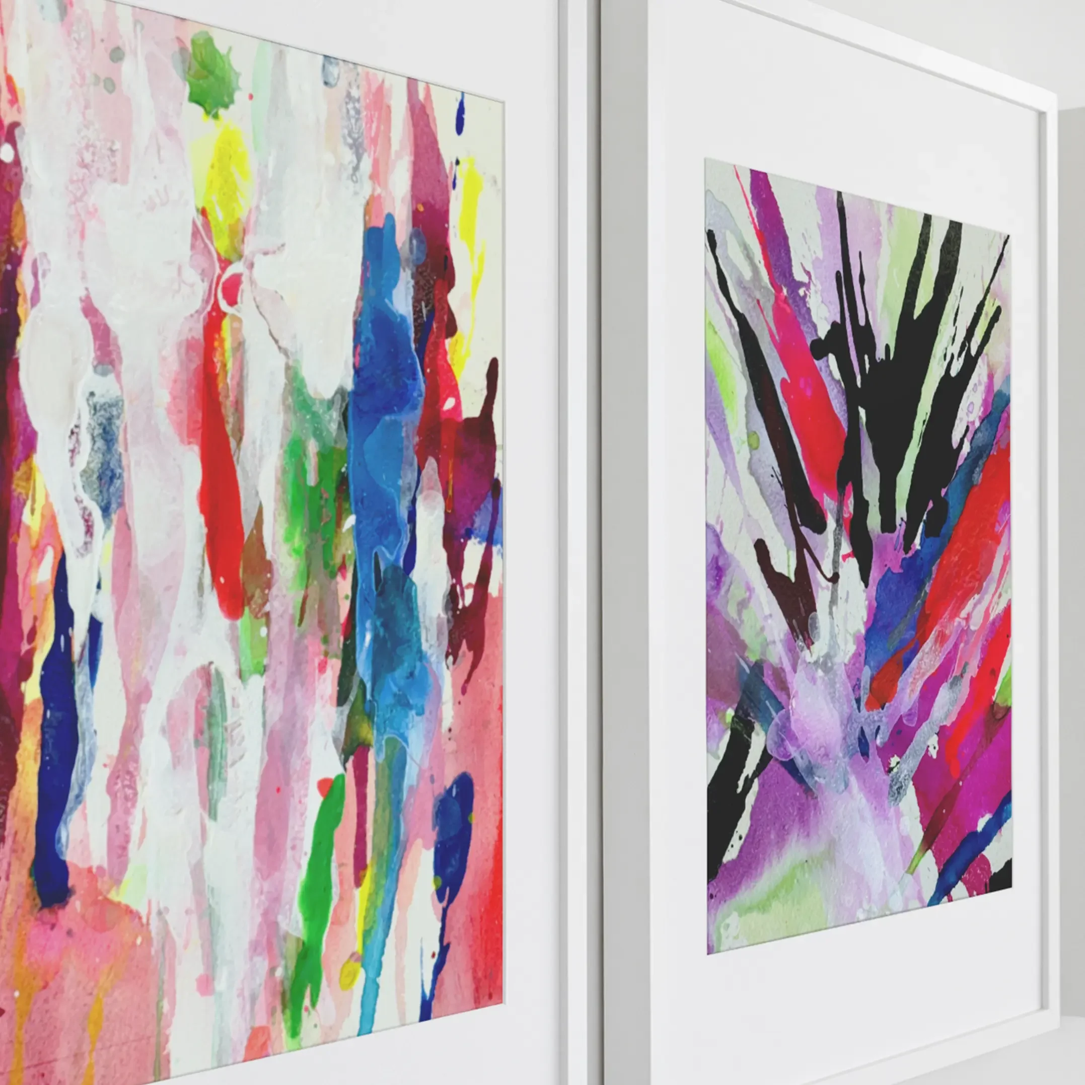 Close up of two framed abstract watercolor paintings featuring pastel pink drips and a bold black burst with vibrant pink, purple, blue, and green strokes in white gallery frames.