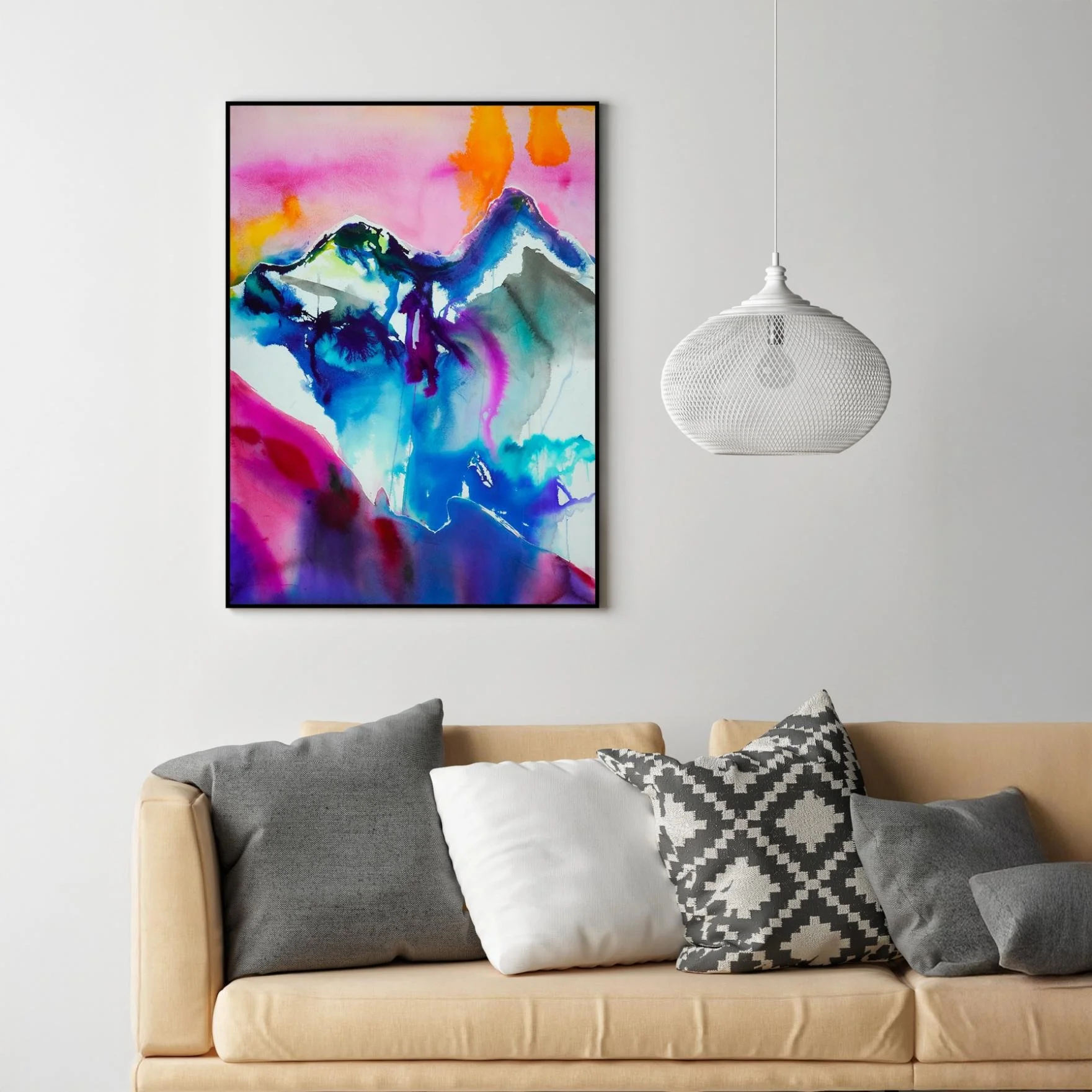 Framed watercolor artwork with bold abstract mountain shapes in magenta, cyan, and orange, hung above a beige couch with monochrome pillows—perfect for modern eclectic home decor.