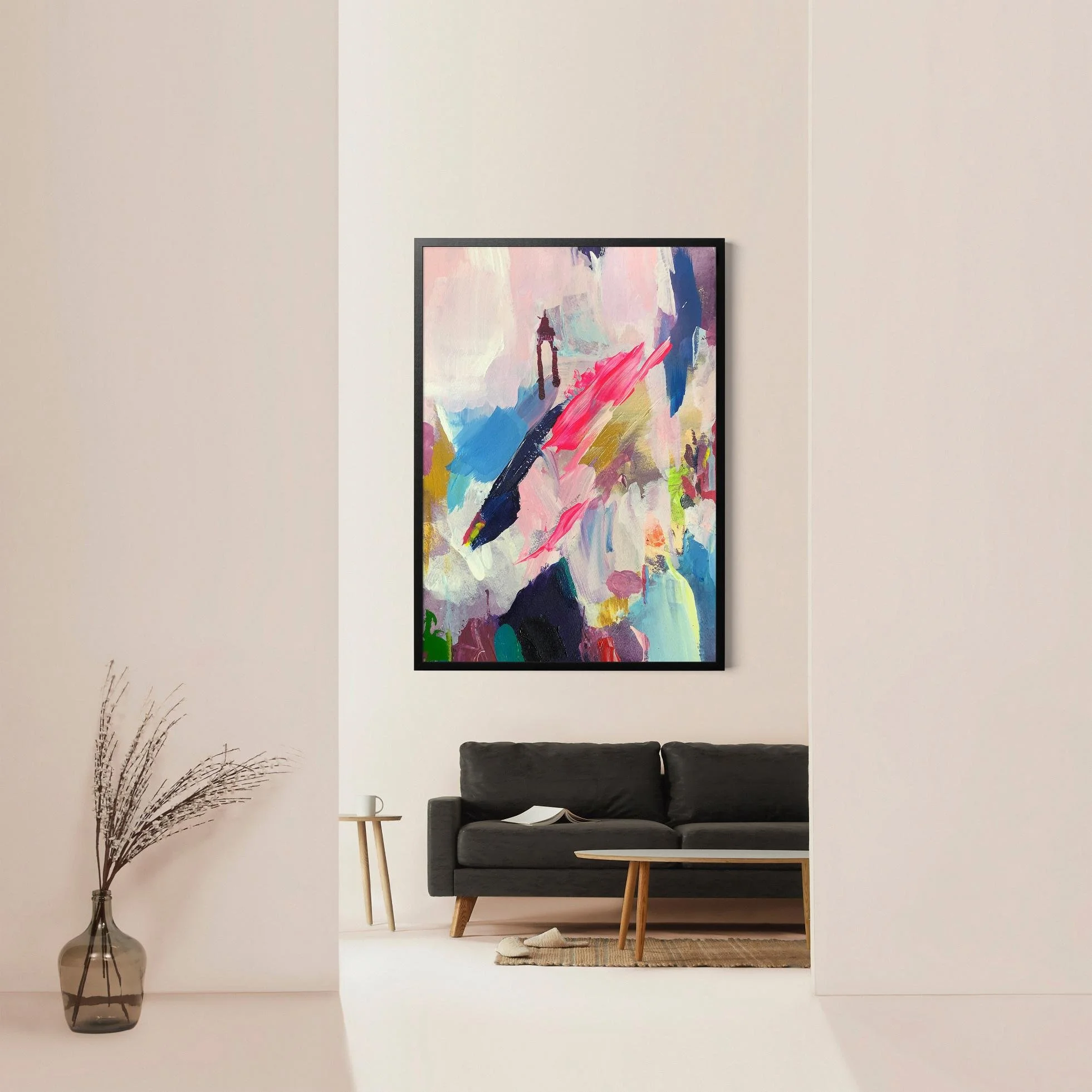 Abstract painting with vivid pink, blue, and gold tones framed in black, displayed above a modern black sofa in a minimalist, high-ceilinged room.