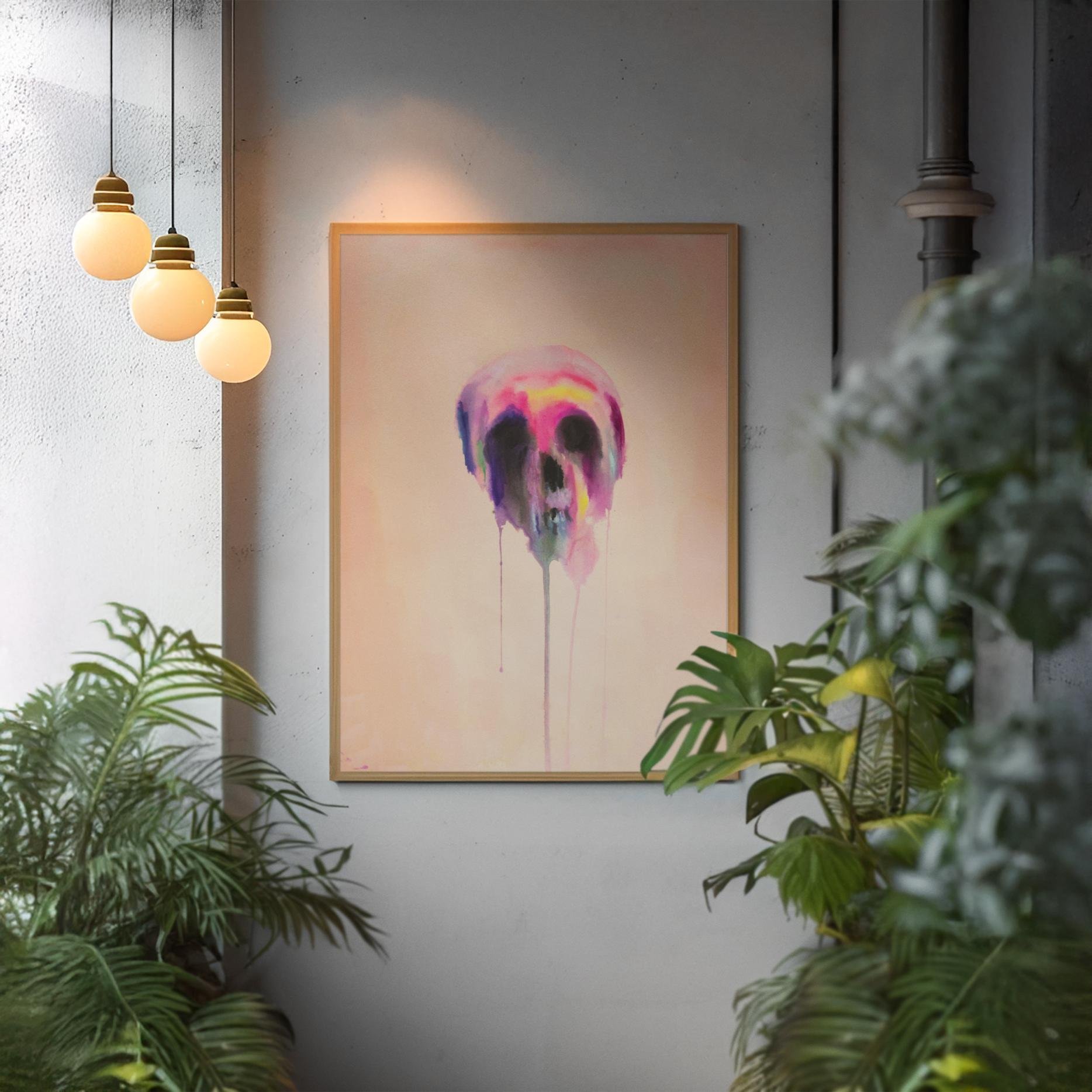 Framed colorful skull painting with long vertical drips, hanging among warm lighting and lush greenery.