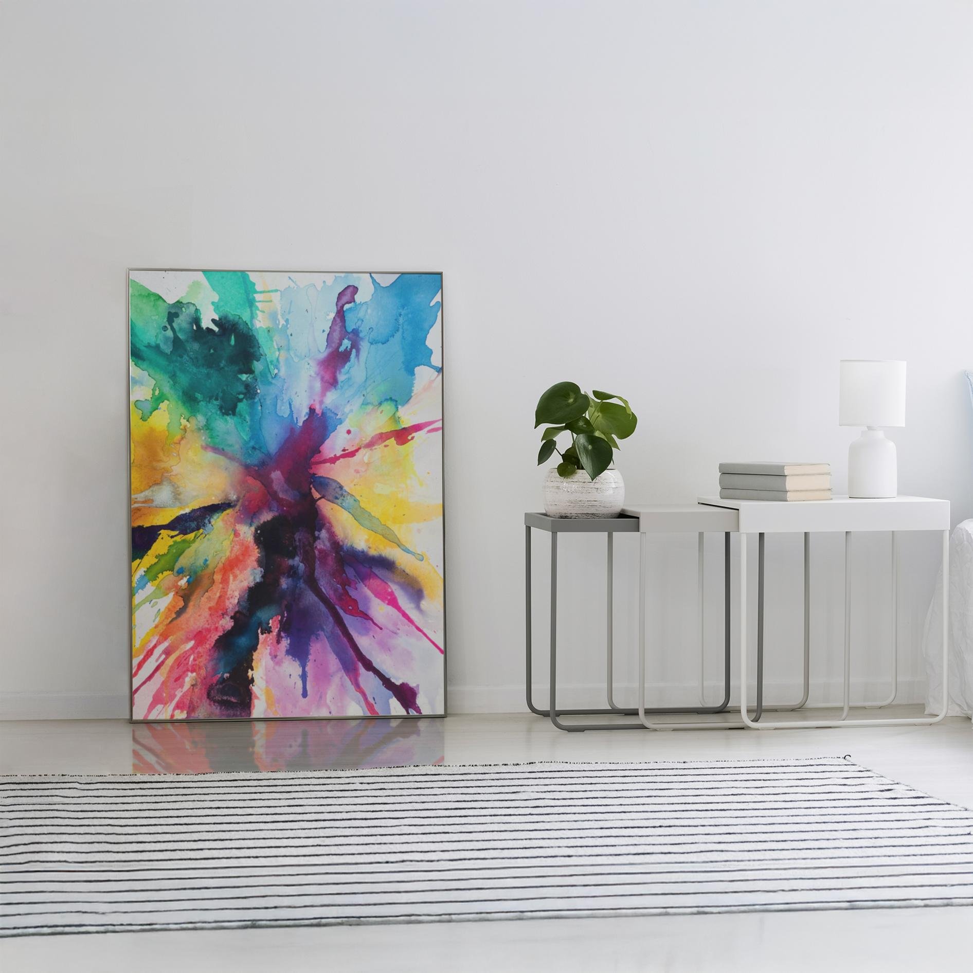 The painting rests on the floor in a white minimalist room beside a small modern console table, with a striped rug and soft natural lighting.