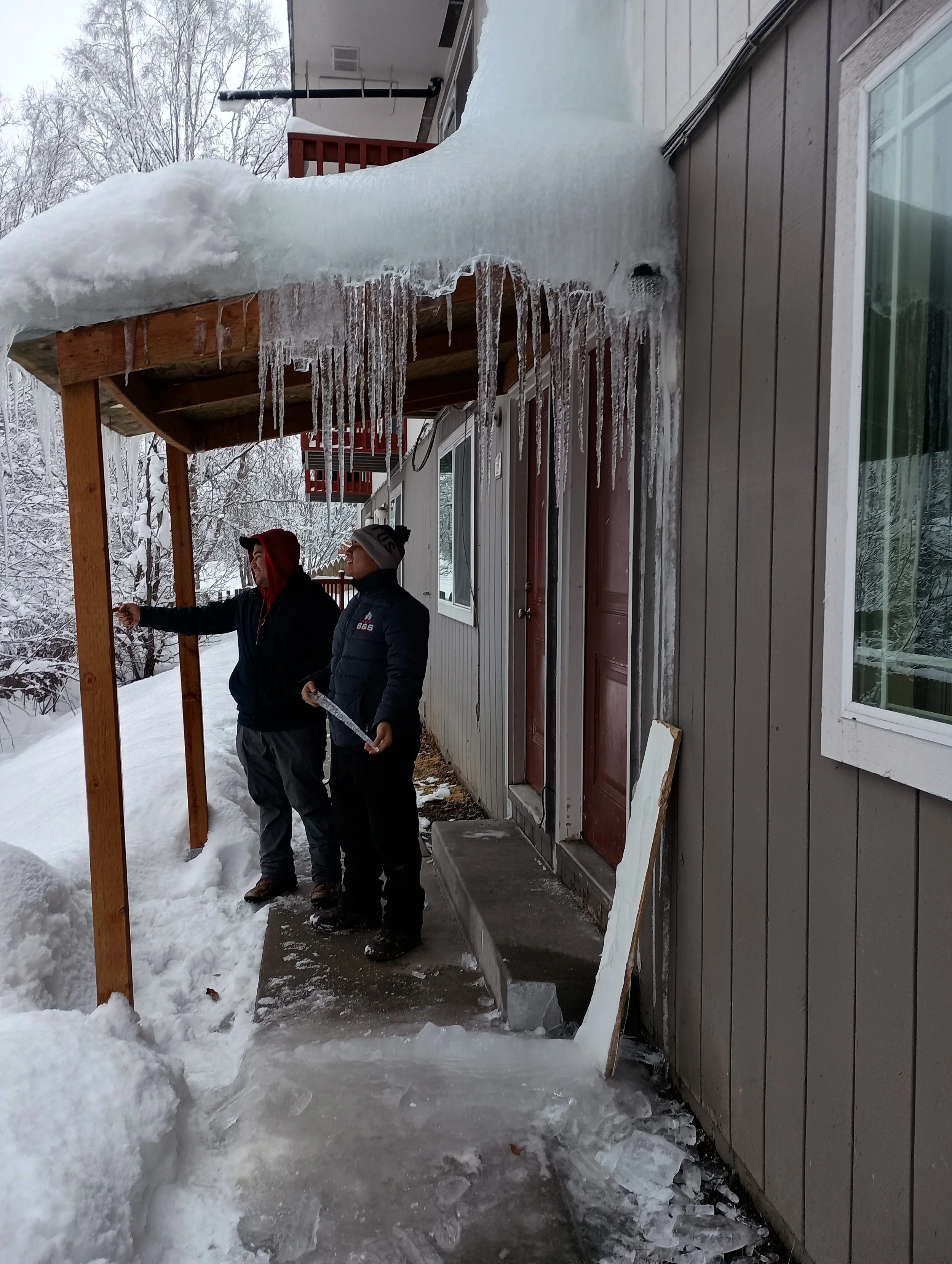 Two people standing under a porch roof with icicles, winter scene