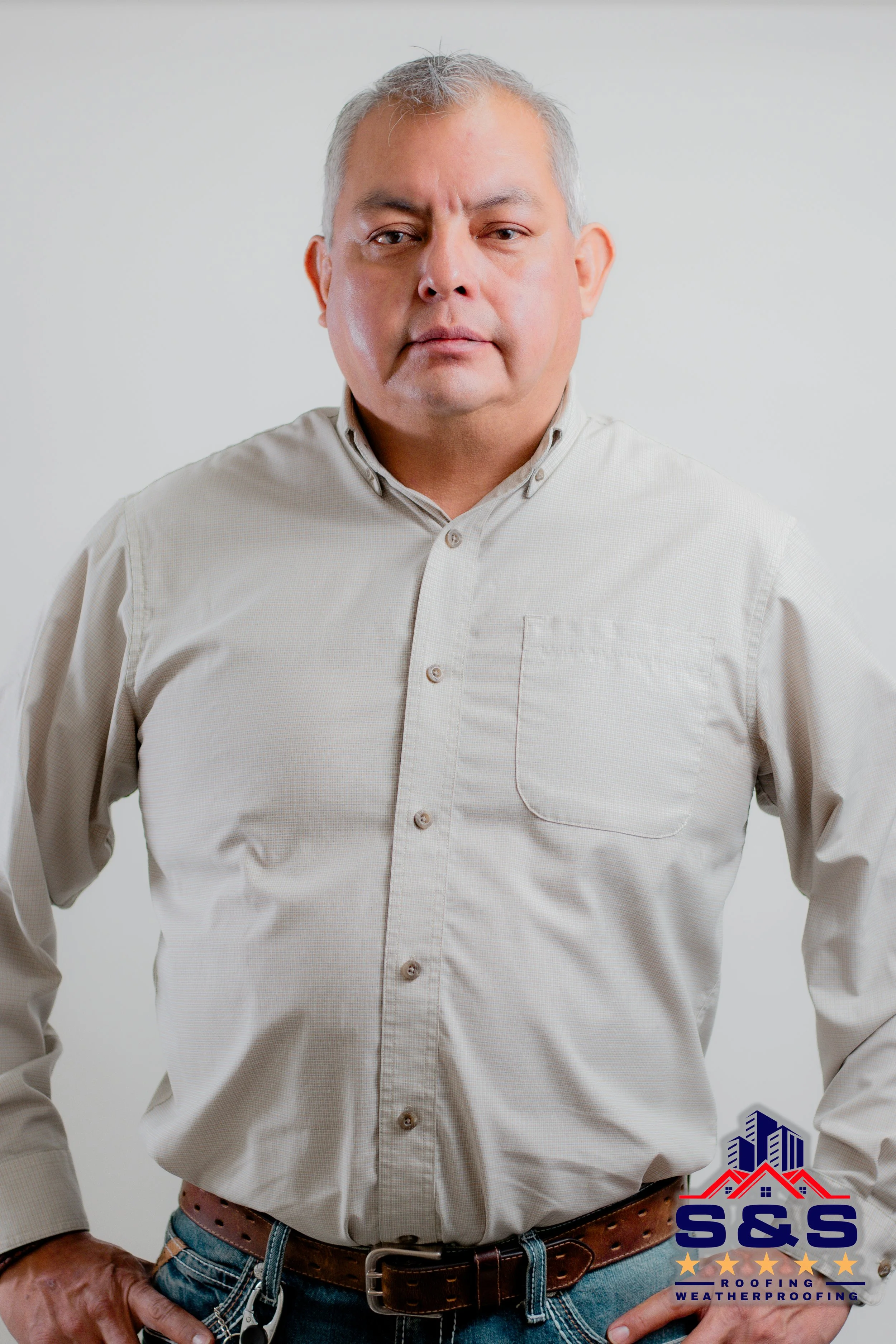 Man smiling, holding a folder with "S&S Construction Services" logo, wearing a light-colored shirt with a matching badge.