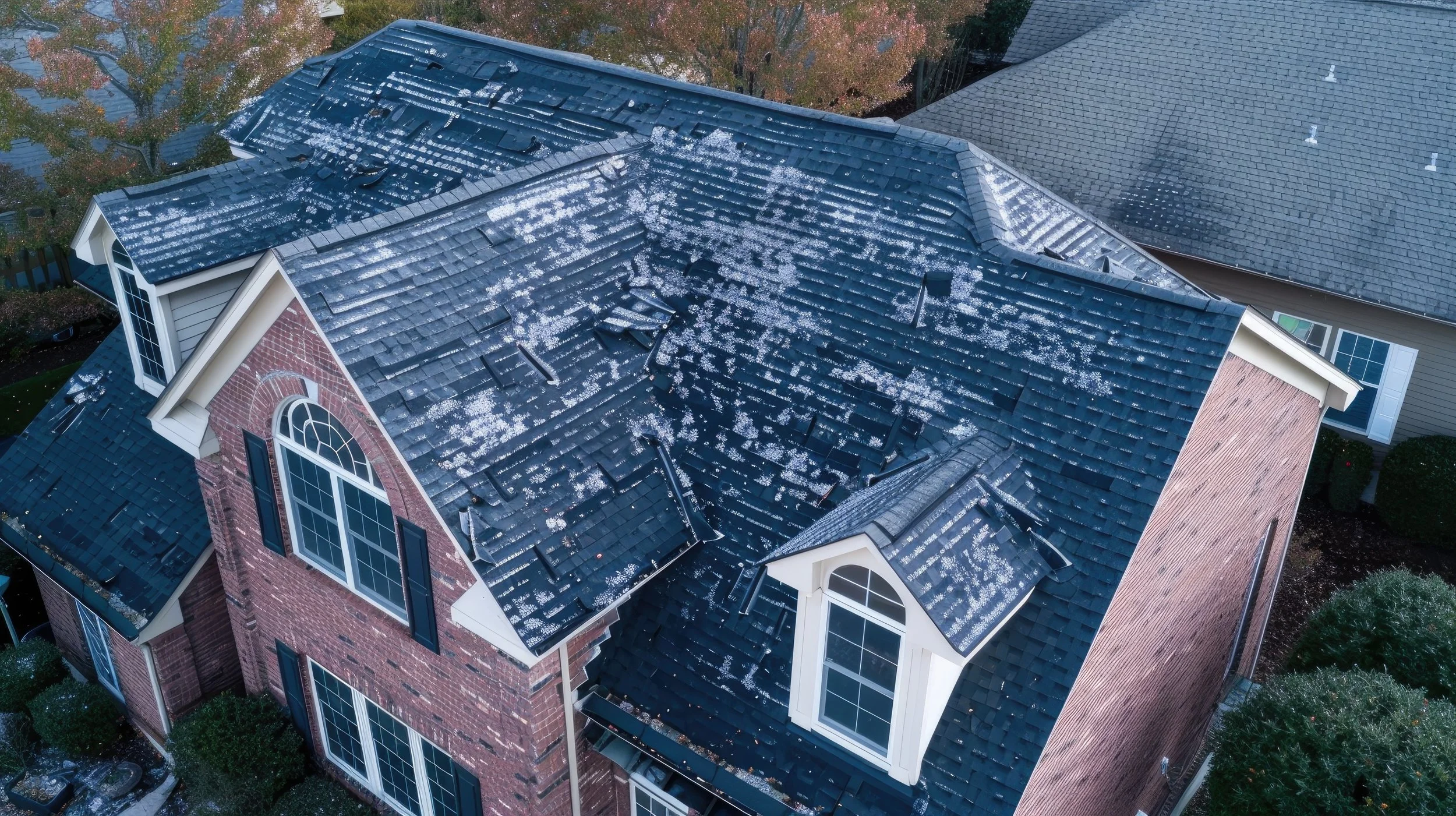Aerial view of a house with a damaged and missing shingles on the roof, indicating storm or hail damage.