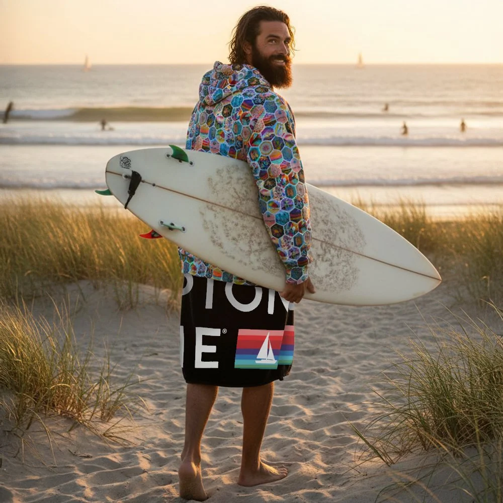 man with surf board. Hamptons Hippie logo beach towel, oversized with a vibrant multi color logo, made from a sustainable cotton-poly blend.
