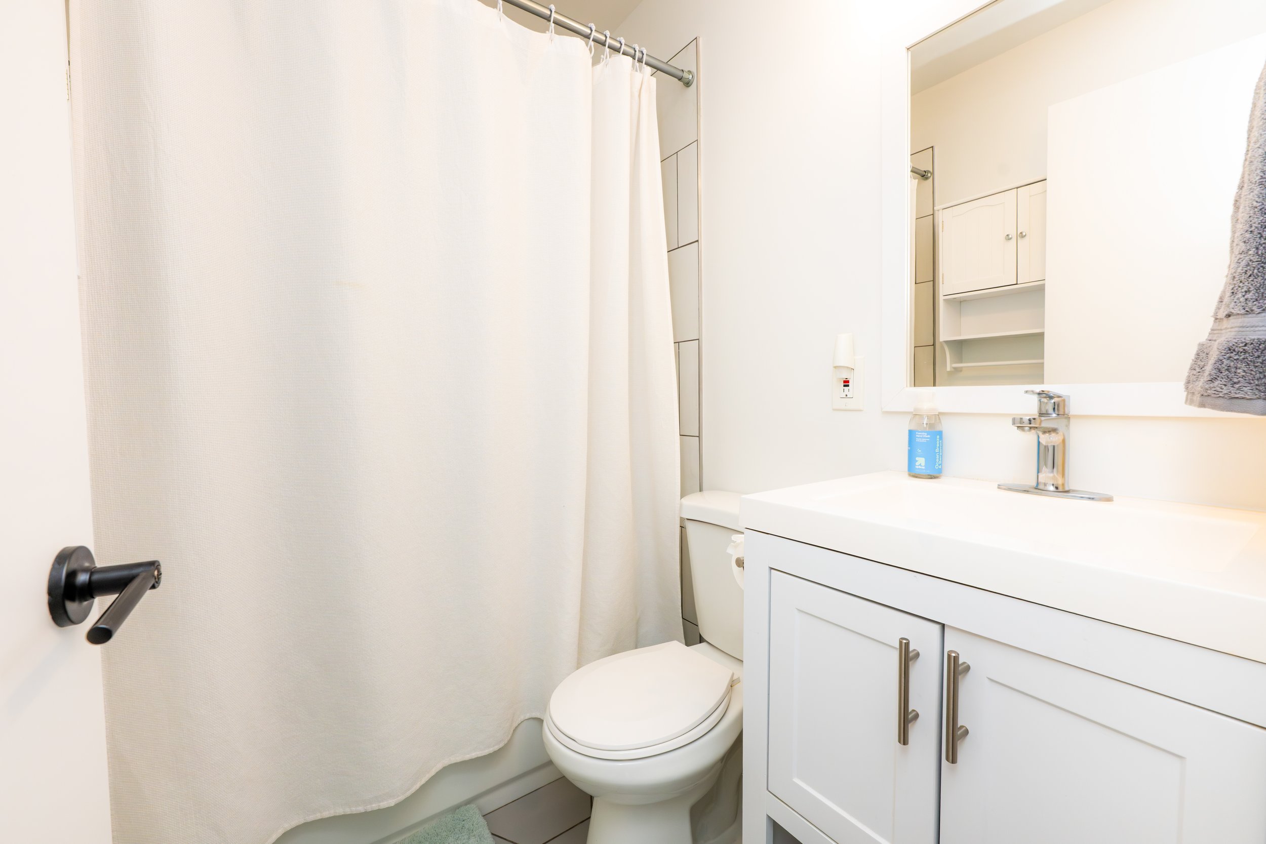 A small bathroom with a white shower curtain, a toilet, a white vanity with a sink, mirror, and a towel hanging on the wall.
