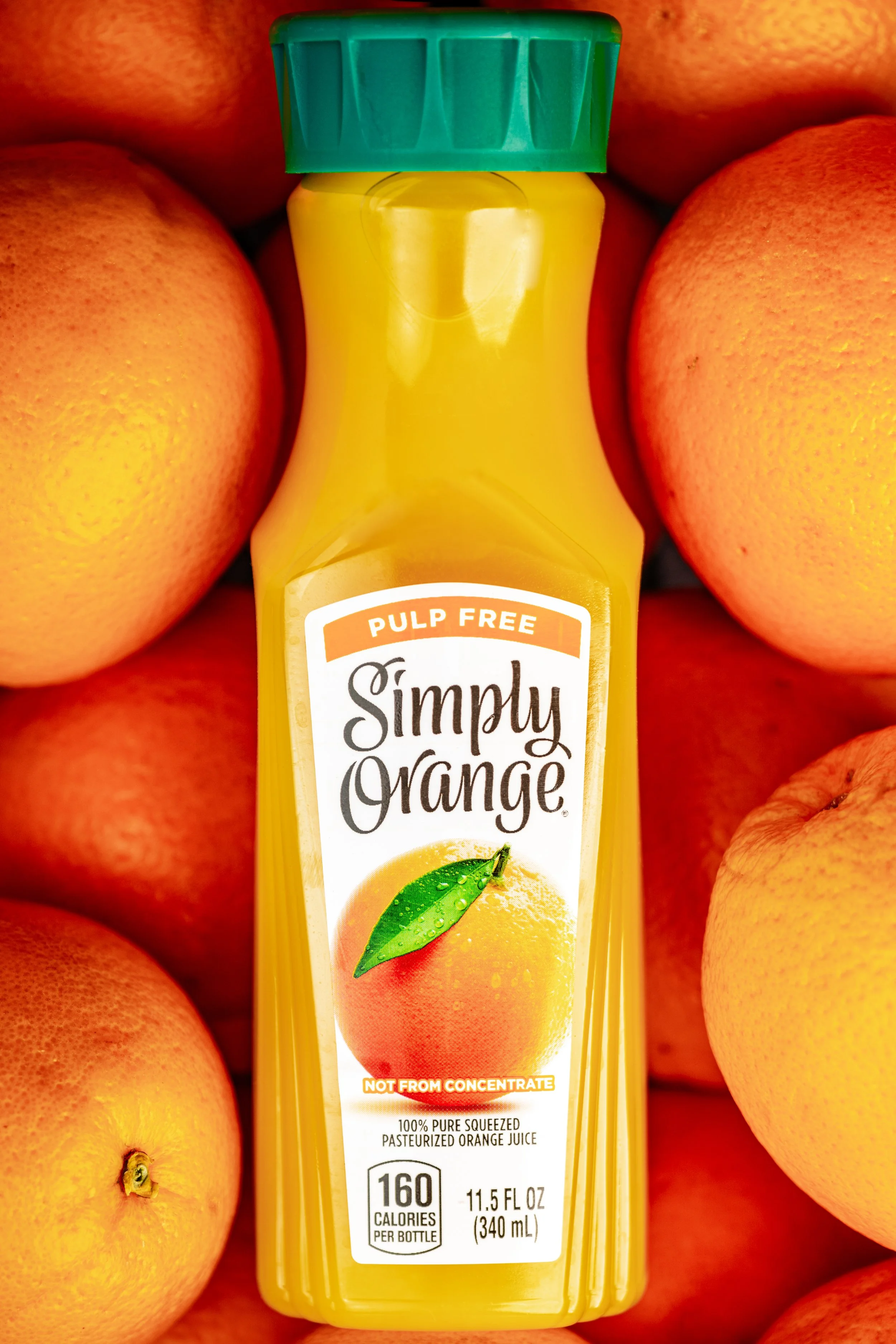 A bottle of Simply Orange pulp-free orange juice surrounded by fresh oranges.
