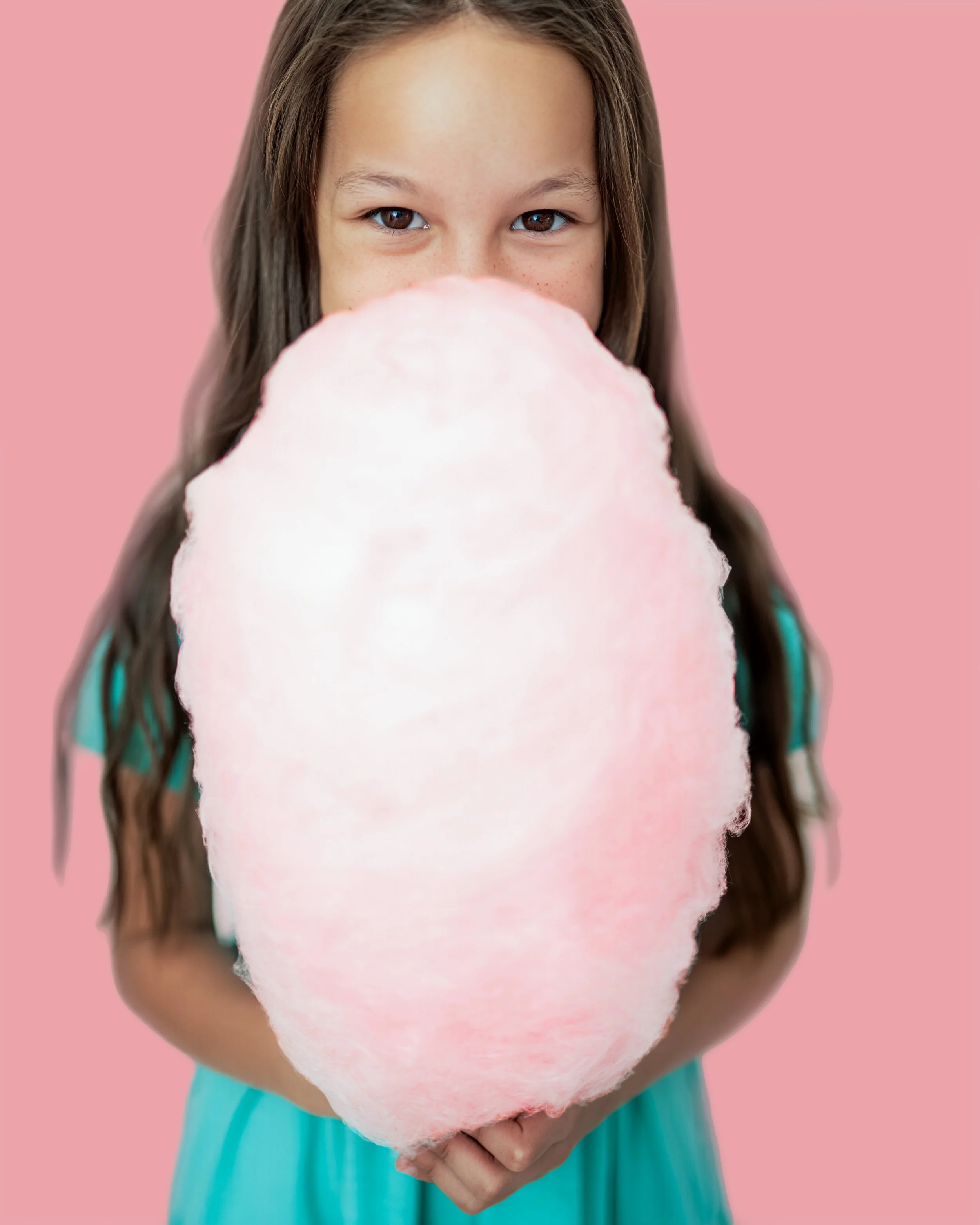 Girl holding large pink cotton candy in front of her face, with a pink background.